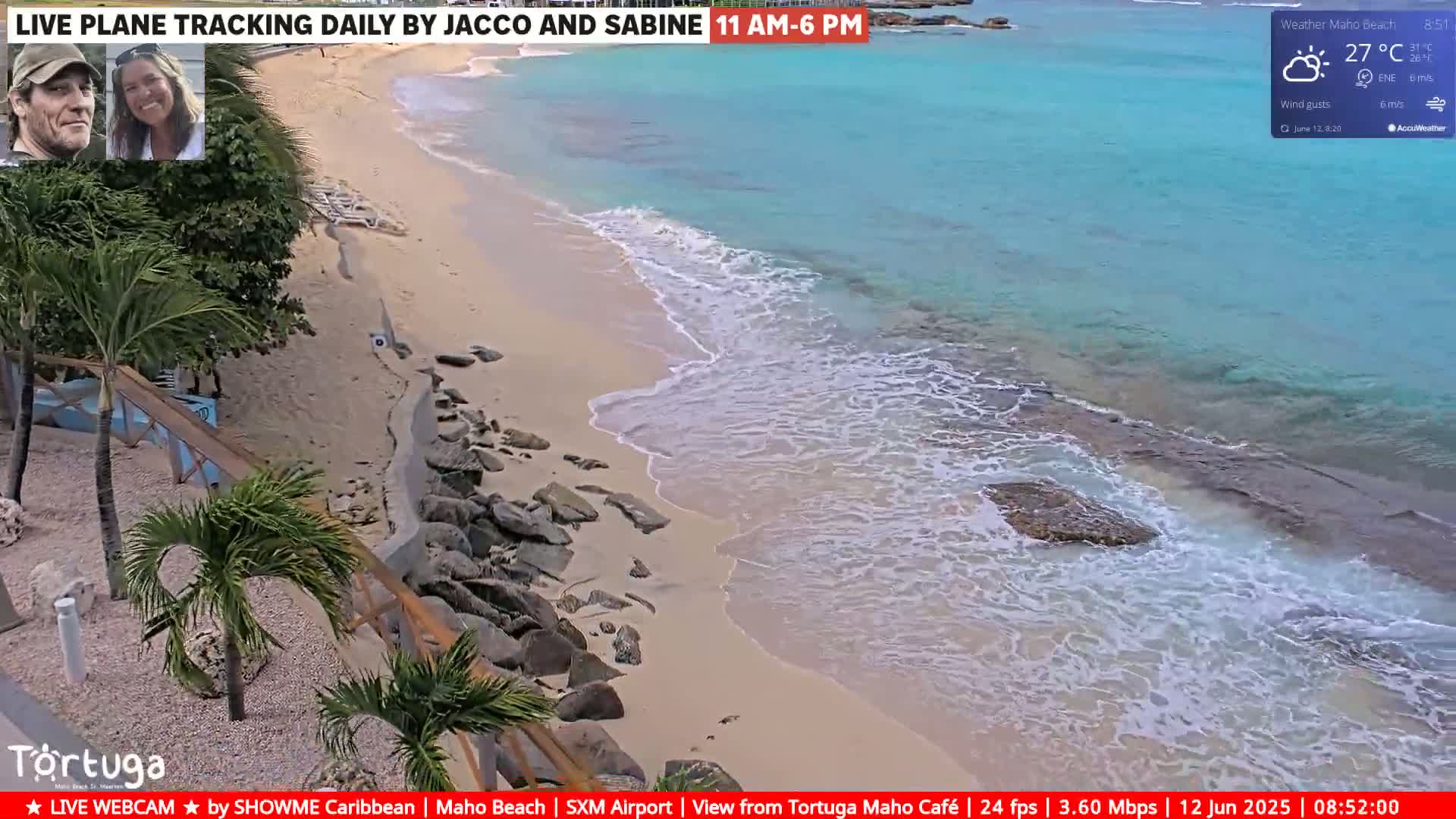 A sandy beach with calm, turquoise water laps gently on the shore, partially obscured by rocks and vegetation on the land.
