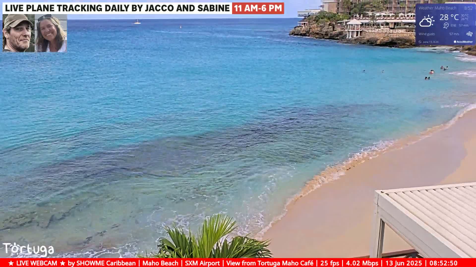 A partly cloudy, sunny day shows a tranquil beach with clear, turquoise water lapping a sandy shore, and several people swimming in the ocean.