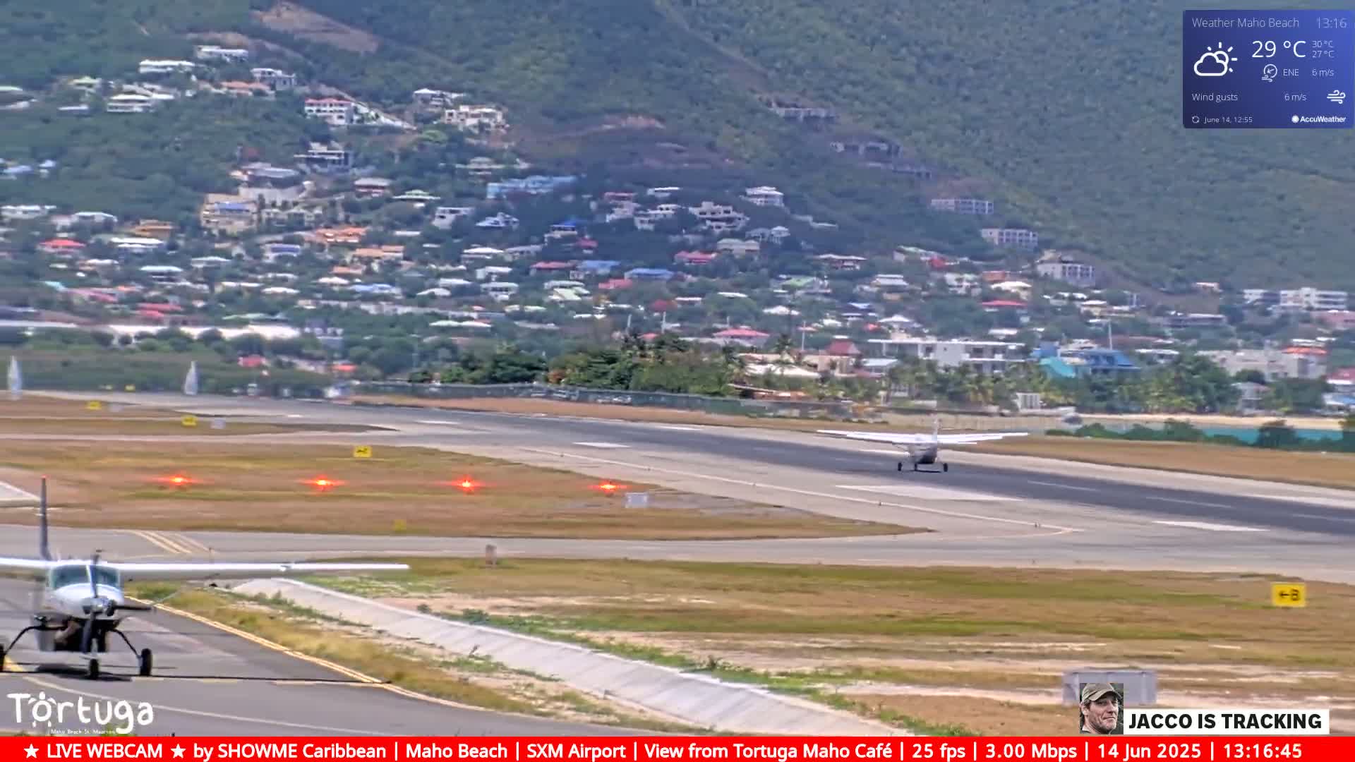 A small airplane taxis on an airport runway near a hillside town under partly cloudy skies.