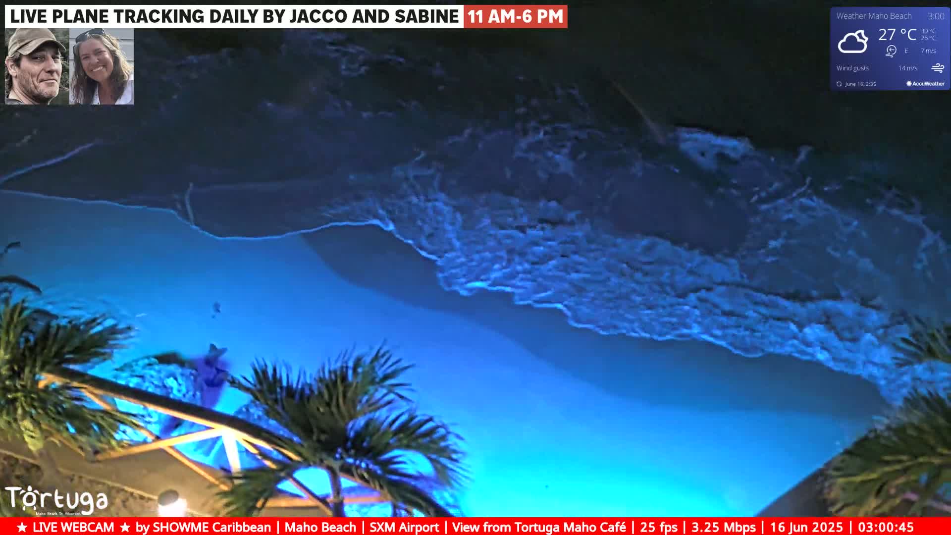 A nighttime, overhead view of ocean waves lapping a beach, illuminated in shades of blue under a partly cloudy sky.
