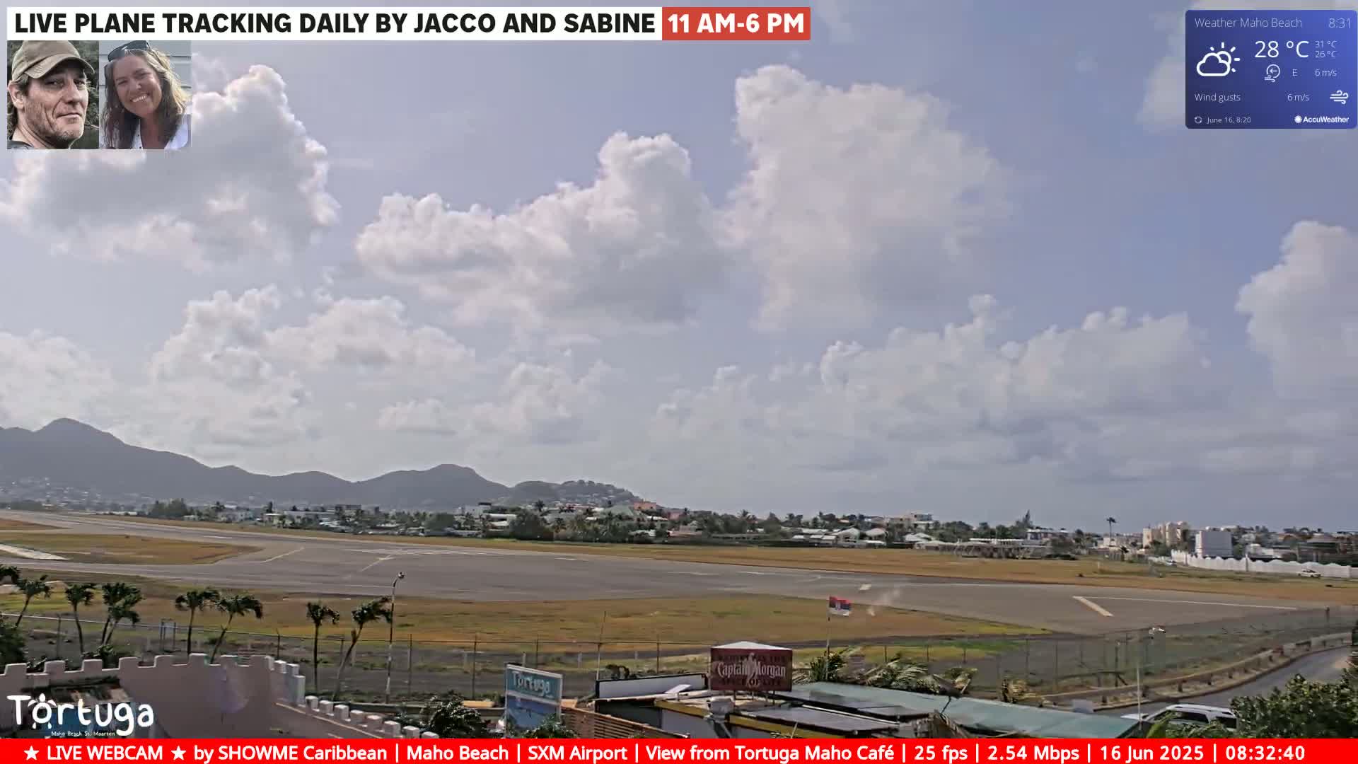 A partly cloudy day at an airport, with a view of a runway, surrounding buildings, and distant hills.