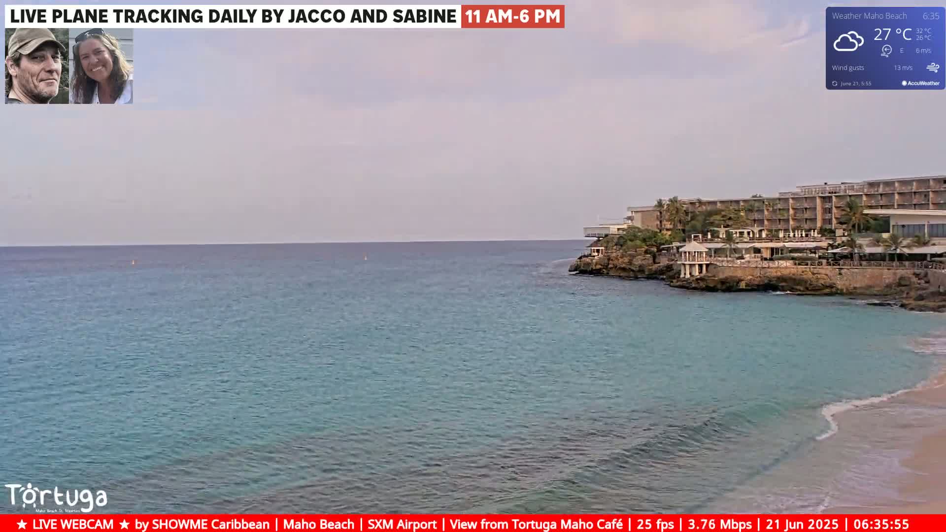 A mostly cloudy day shows a calm ocean with turquoise water lapping a sandy shore near a resort.