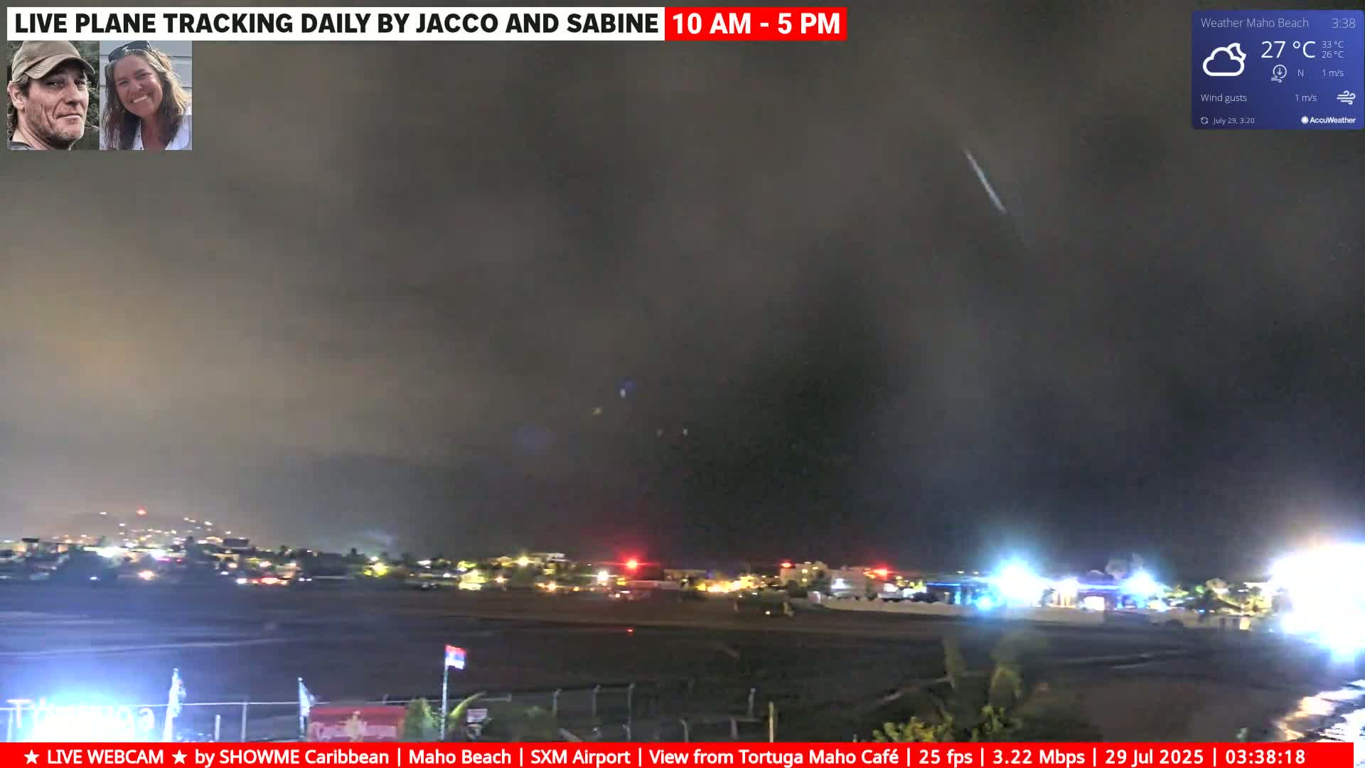 A nighttime view of an airport runway and surrounding buildings under a dark, cloudy sky with a slight wind.