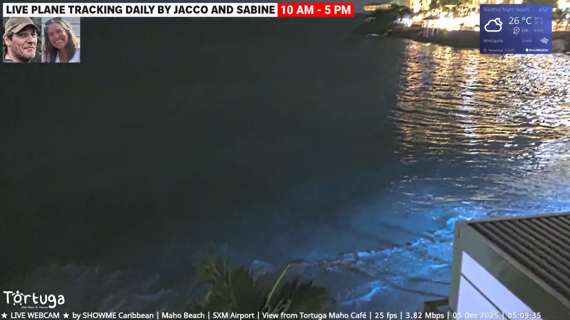 An evening view captures dark, rippling water reflecting numerous distant lights, with the corner of a structure visible in the foreground, under breezy conditions.