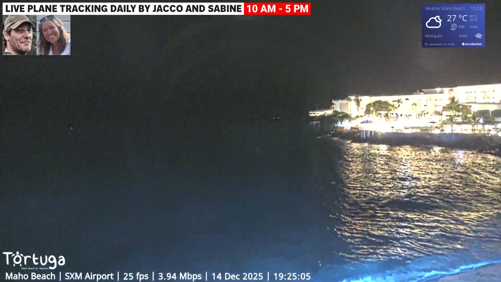 An evening view captures dark, rippling water reflecting numerous distant lights, with the corner of a structure visible in the foreground, under breezy conditions.