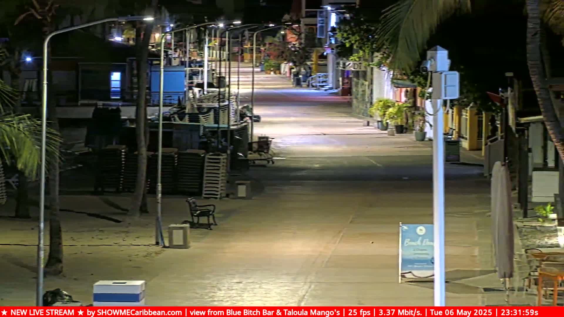 A mostly empty, brightly lit pedestrian street at night, lined with closed shops and stacks of beach chairs.