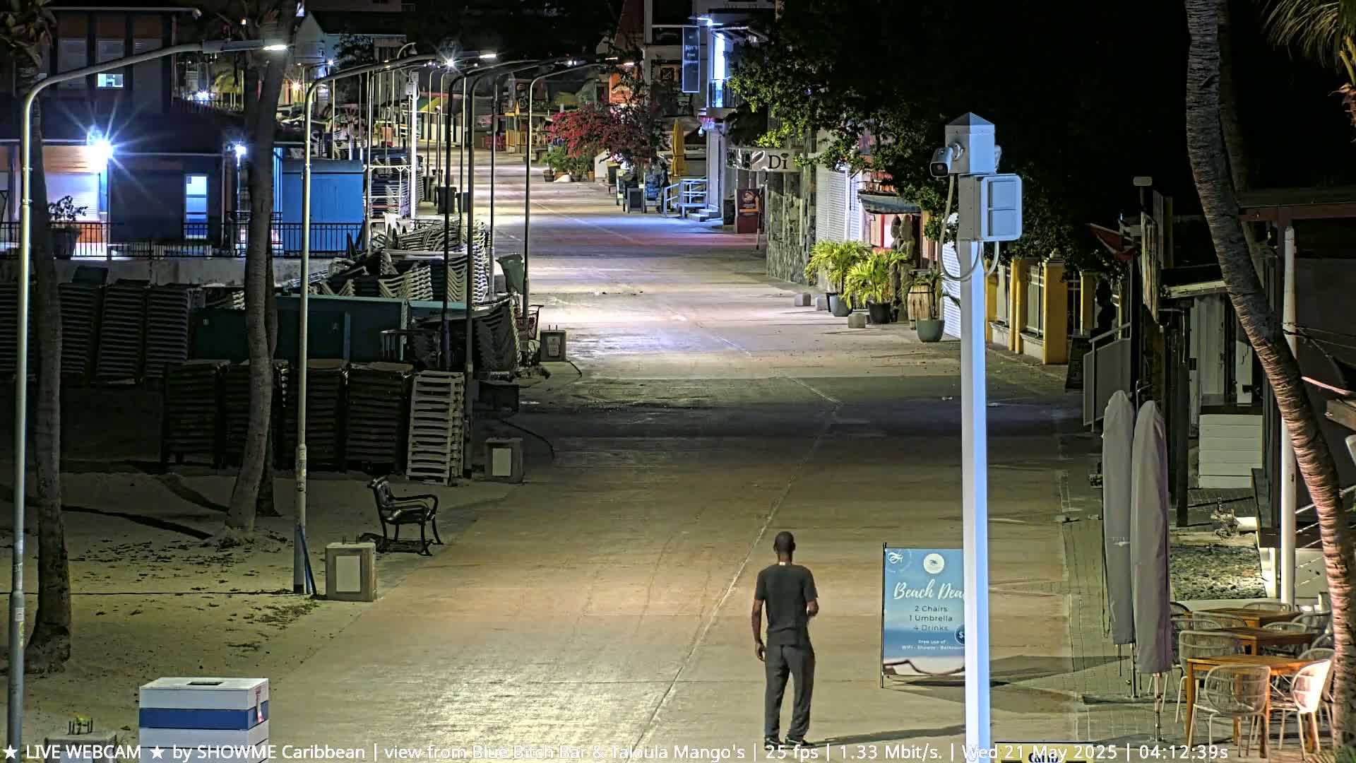 A mostly empty nighttime street lined with buildings and palm trees, with a single person walking down the middle.