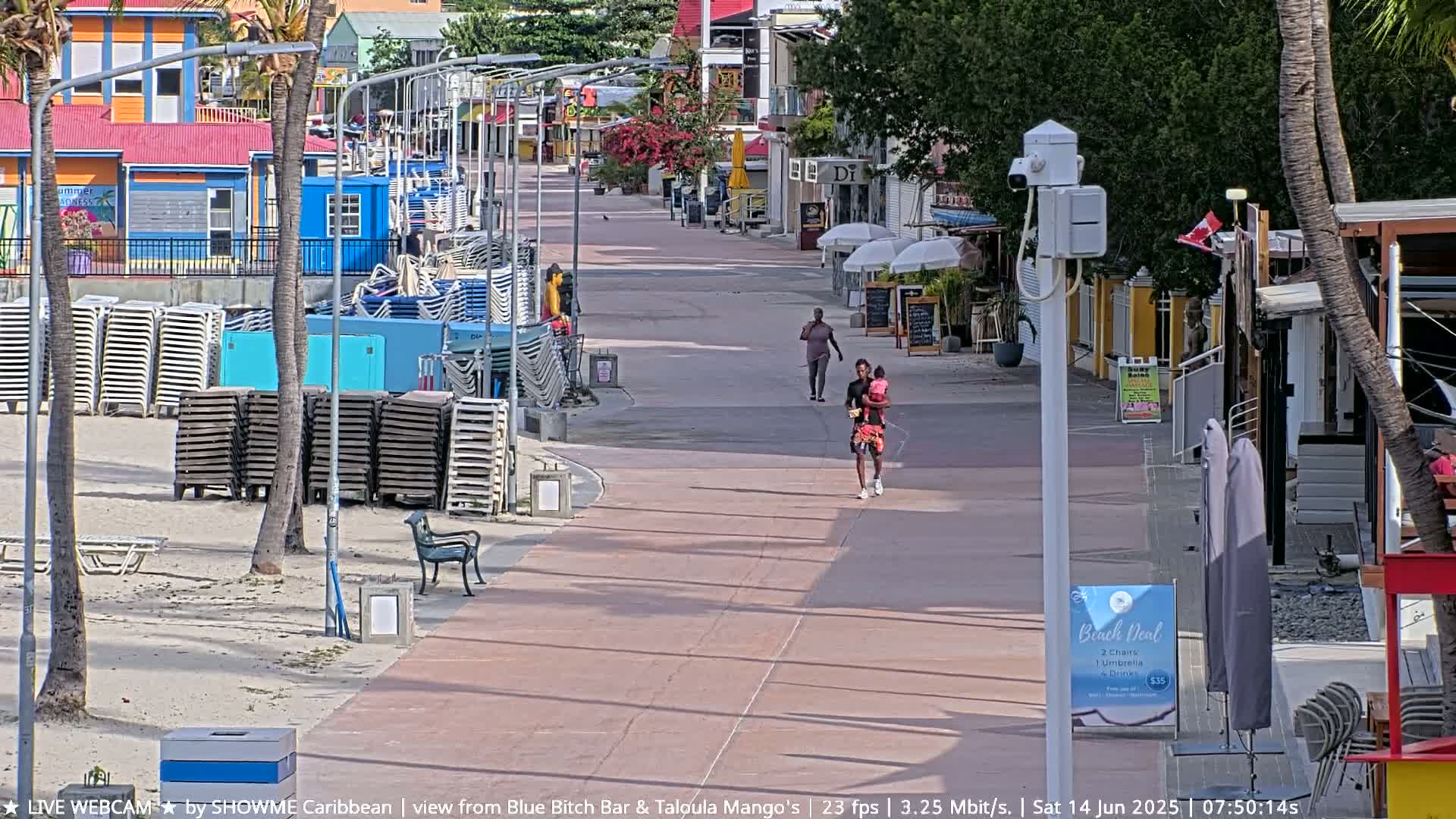 A sunny boardwalk with stacked beach chairs and people walking, lined with colorful buildings.
