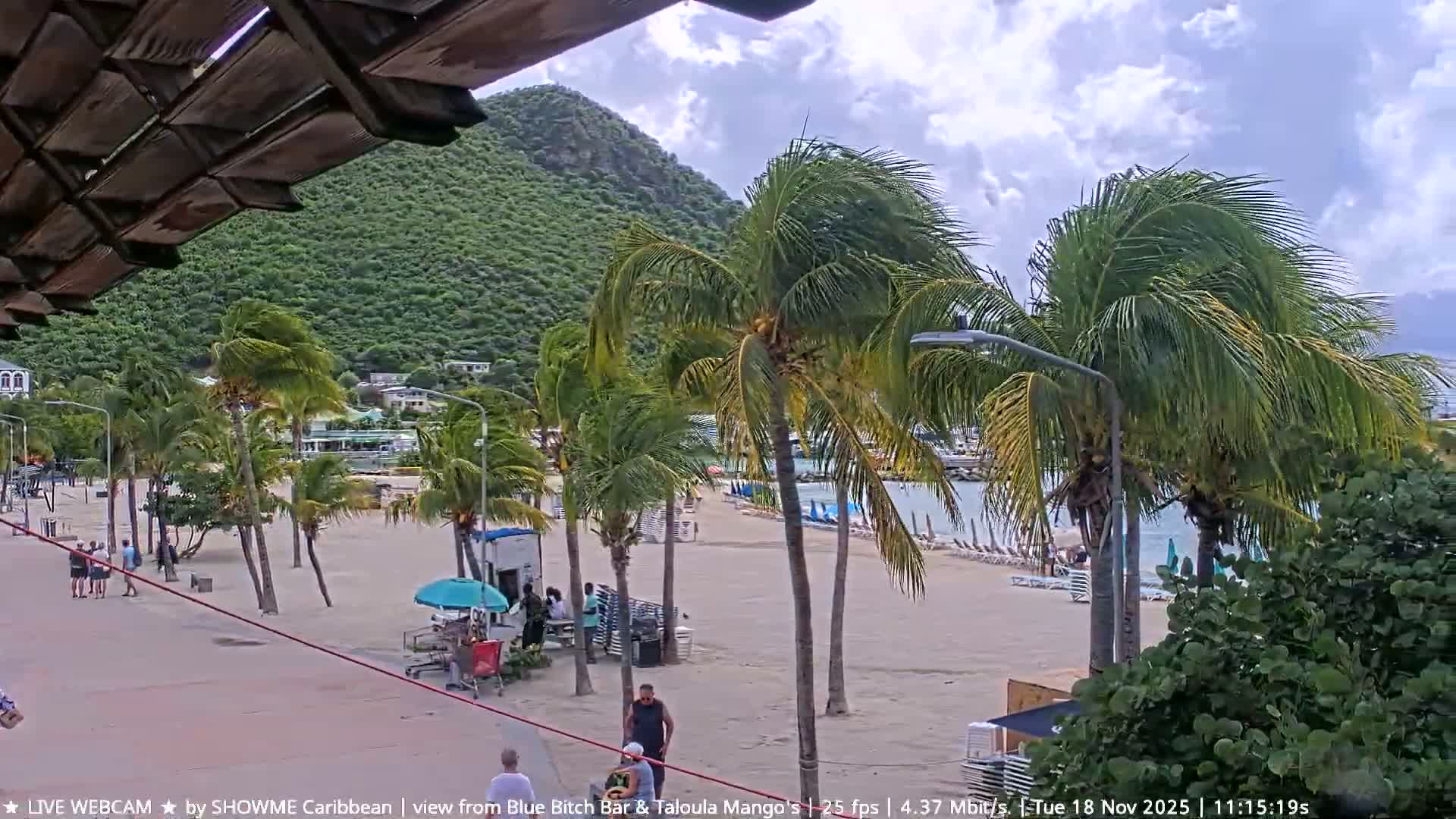 Two men walk along a brightly lit beach promenade lined with stacked chairs and illuminated buildings under a clear night sky.