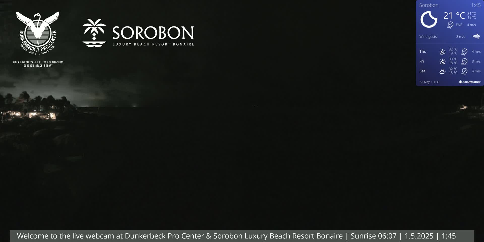 A dark nighttime scene shows a shoreline with a few faint lights, under a mostly clear, dark sky.