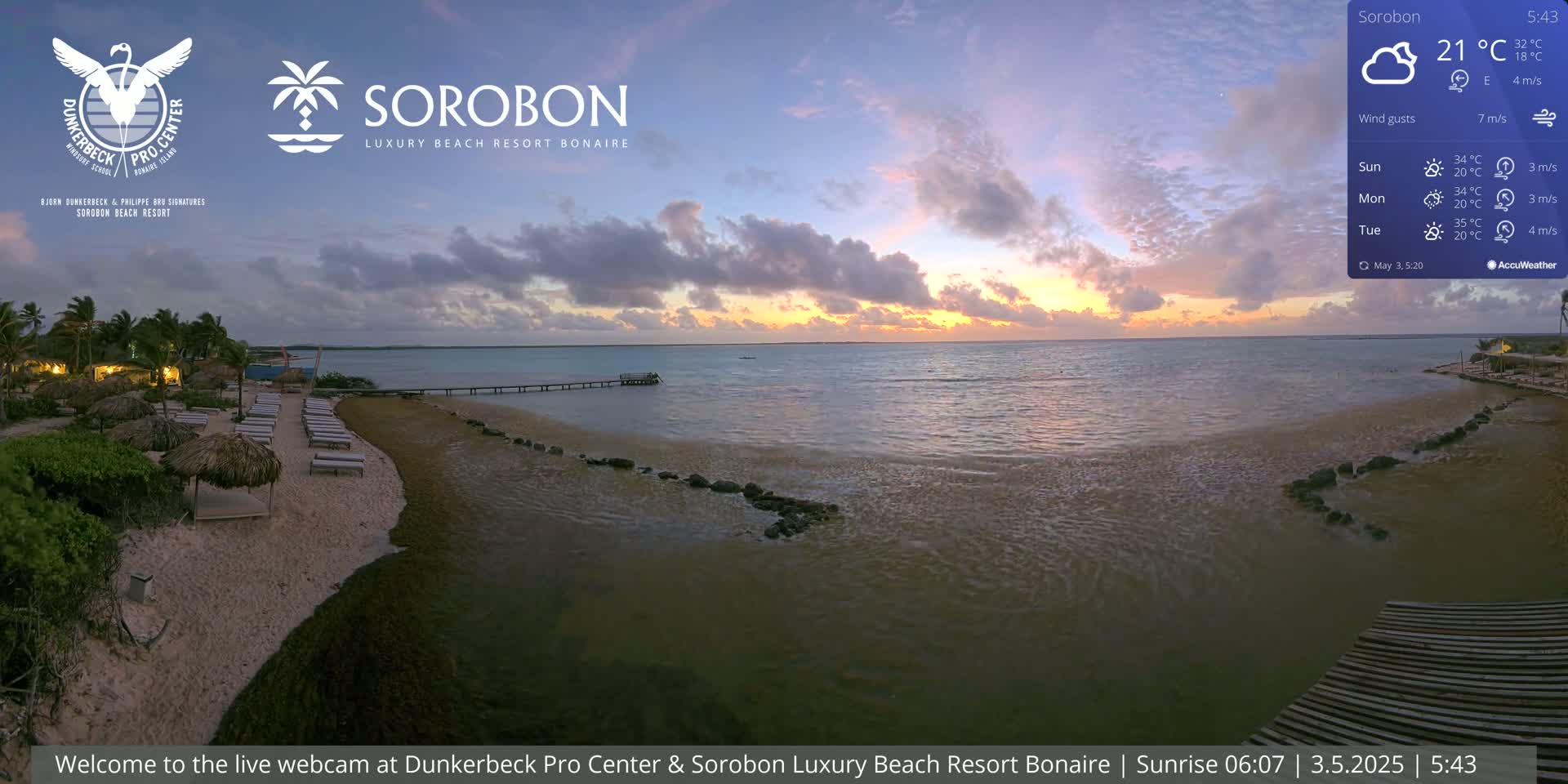 A beach resort at sunrise, with calm water and a partly cloudy sky.