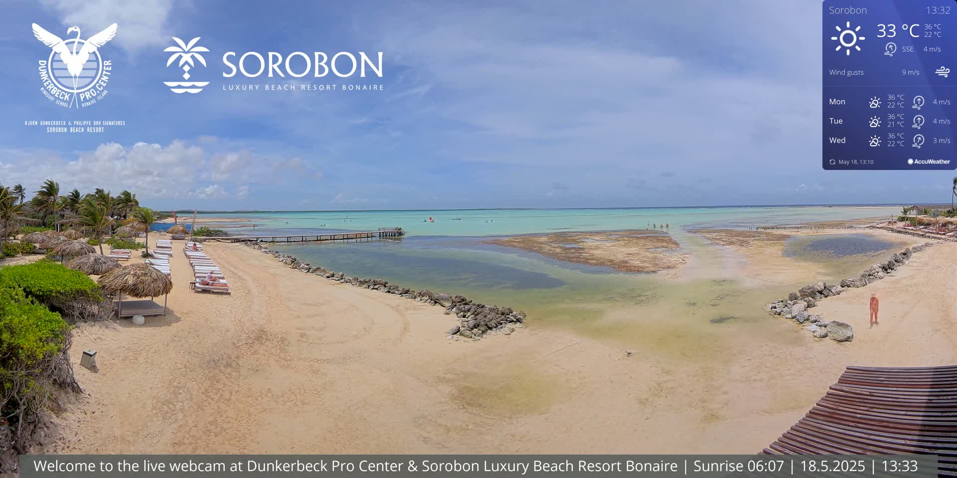 A sandy beach with lounge chairs and umbrellas under a sunny sky overlooks calm, shallow turquoise water.