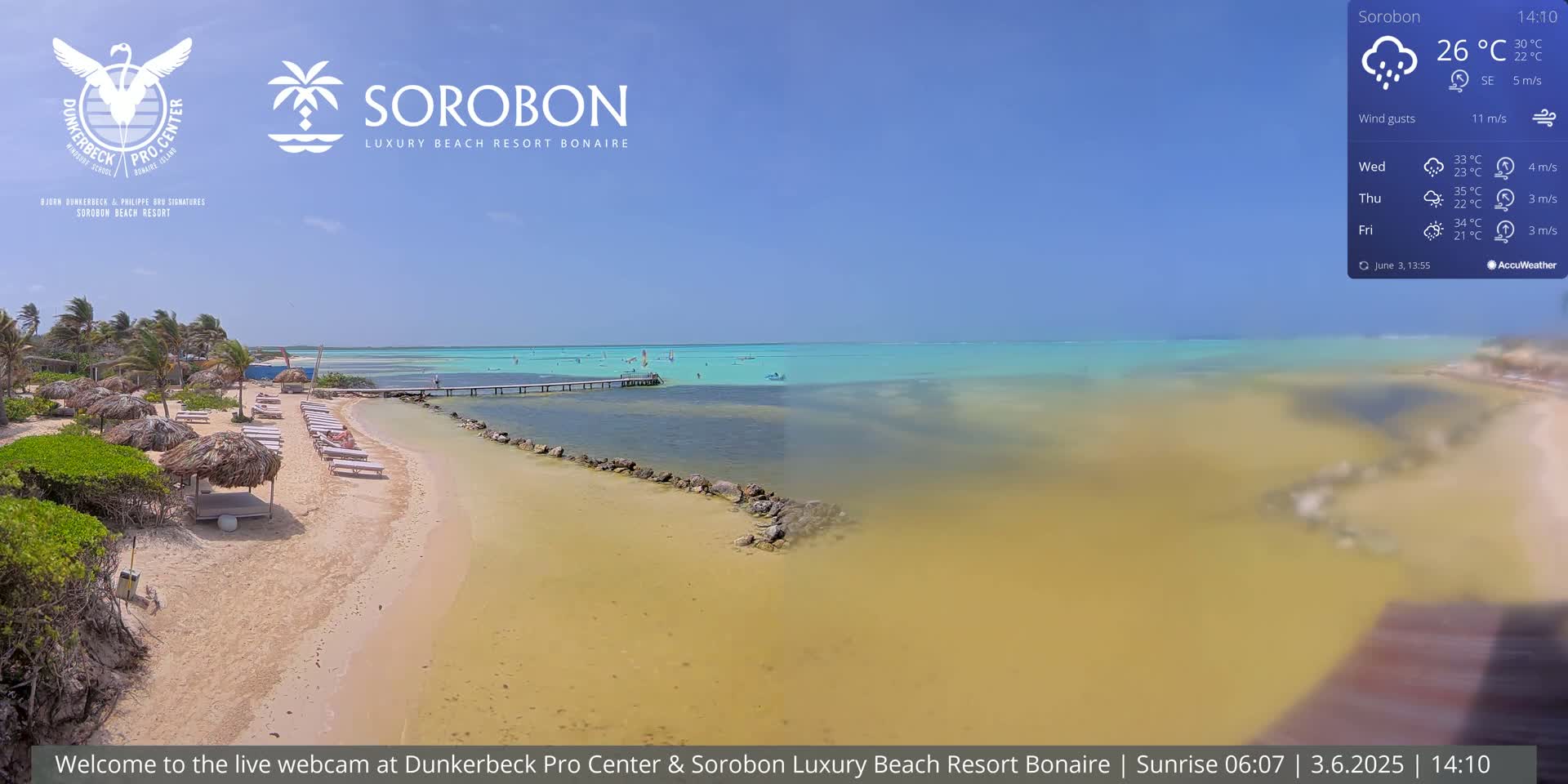 A sandy beach with thatched umbrellas and lounge chairs stretches toward a calm, shallow turquoise sea under a partly cloudy sky.