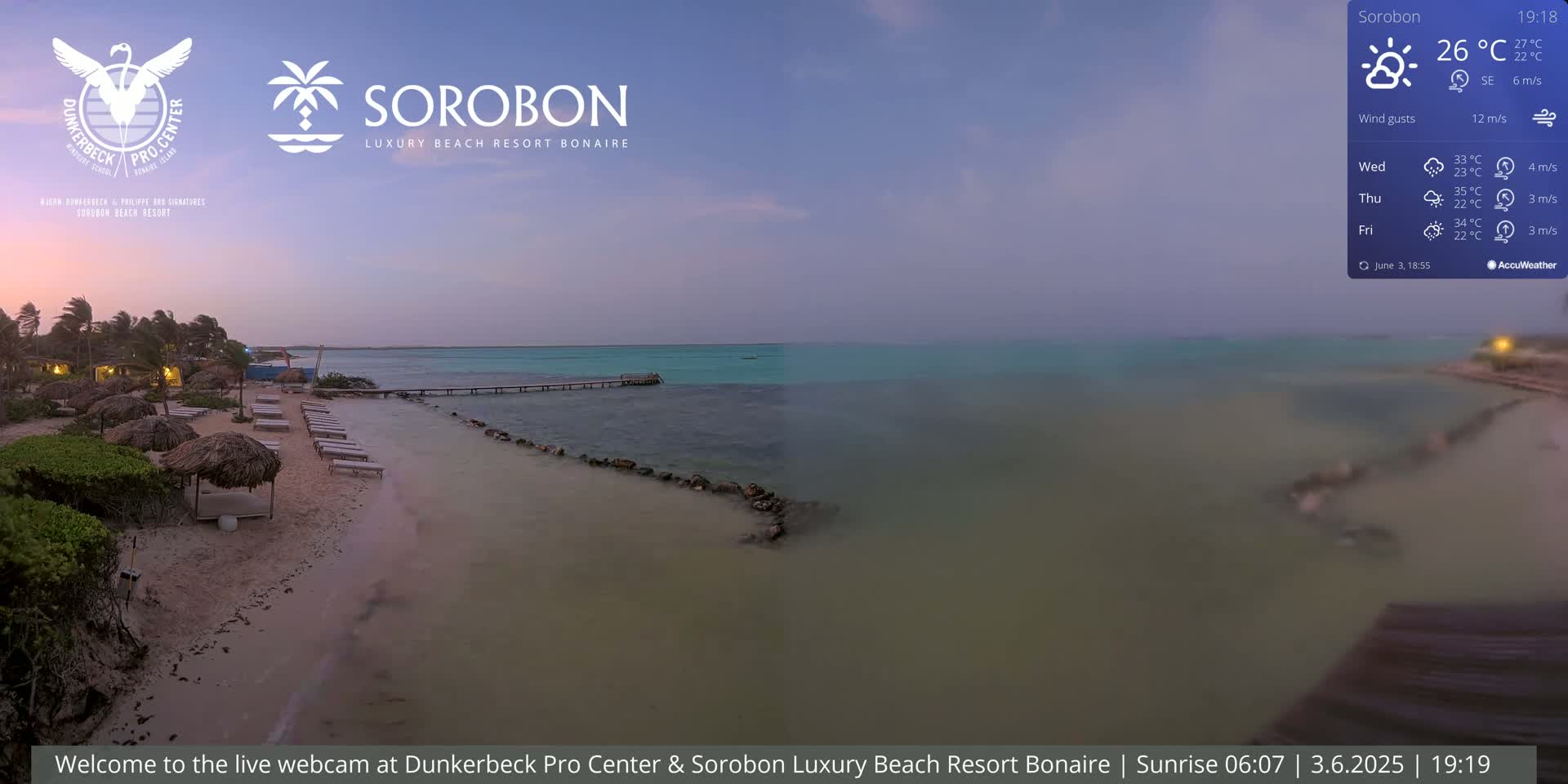 A sandy beach with lounge chairs and thatch umbrellas is shown at dusk, next to calm turquoise water and a small pier, under a twilight sky.