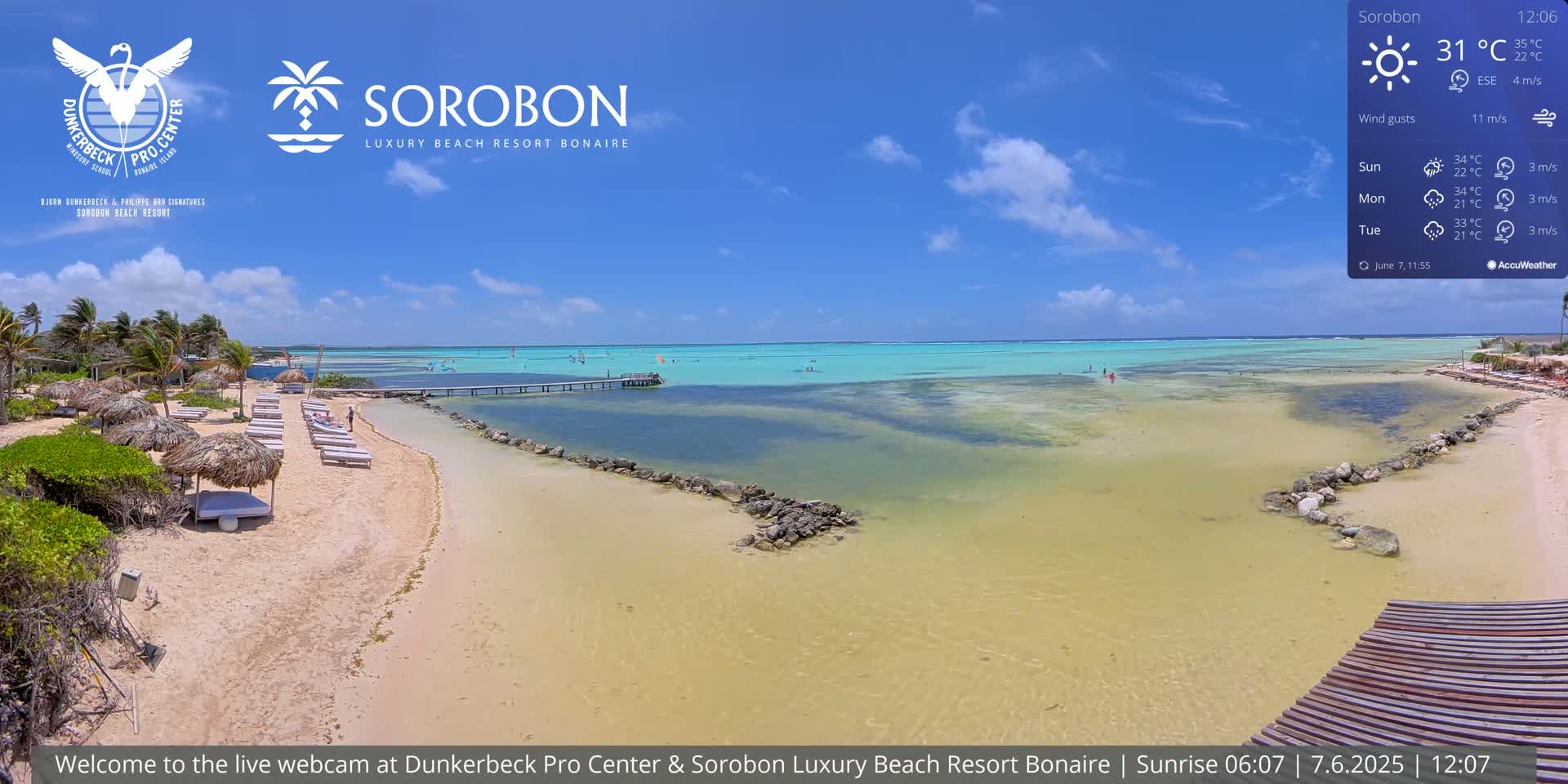 A sandy beach with thatched umbrellas and lounge chairs, a calm turquoise ocean, and a partly cloudy blue sky.