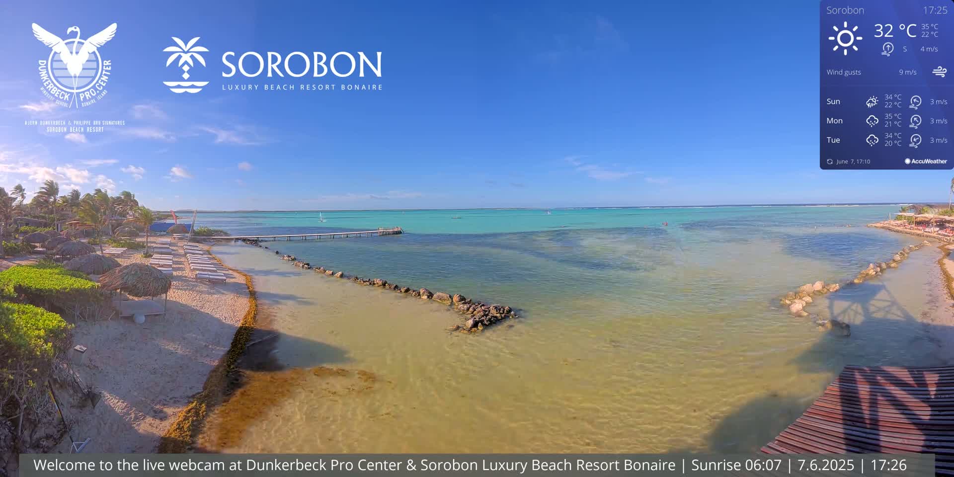 A sandy beach with lounge chairs and umbrellas stretches to a calm, turquoise ocean under a clear blue sky.