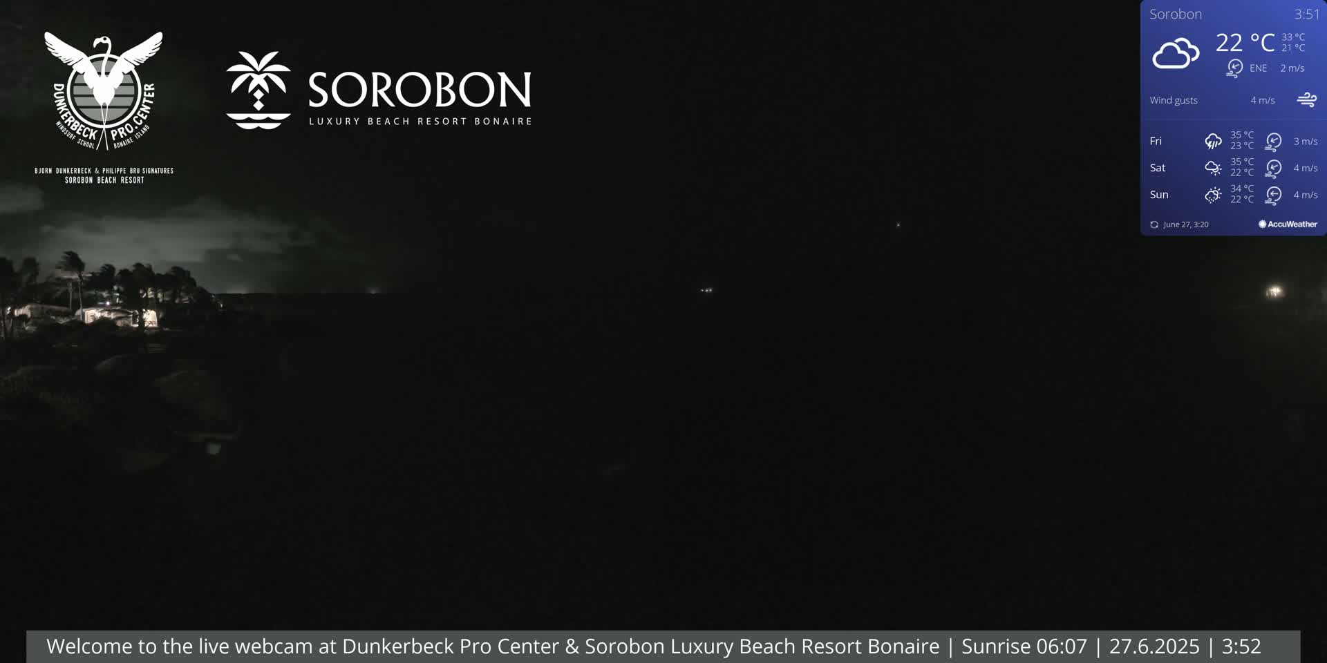 A nighttime view of a dark coastline with a few faint lights visible, under cloudy skies and a light breeze.