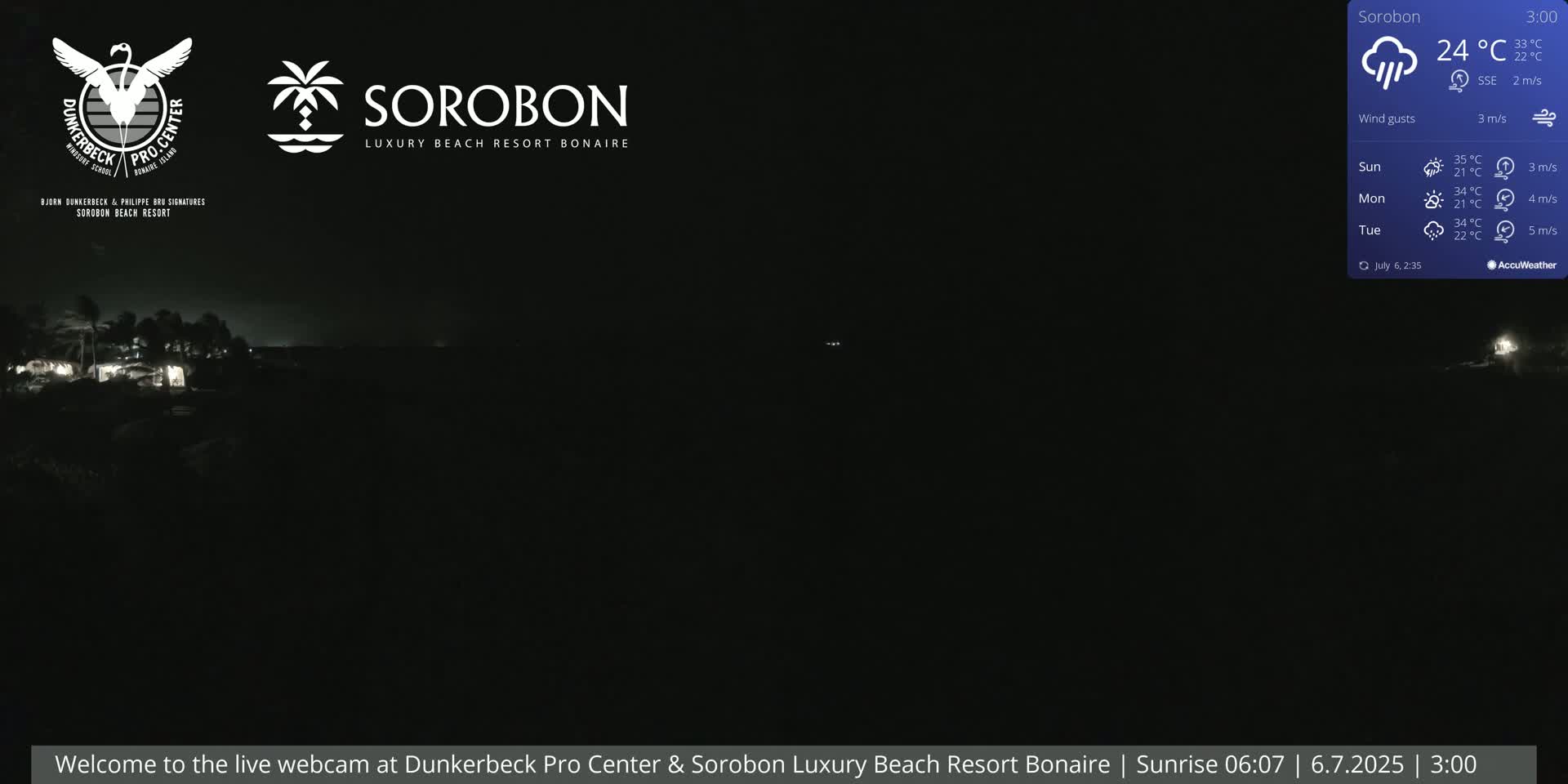 A nighttime view of a dark beach with a few distant lights, under cloudy conditions.