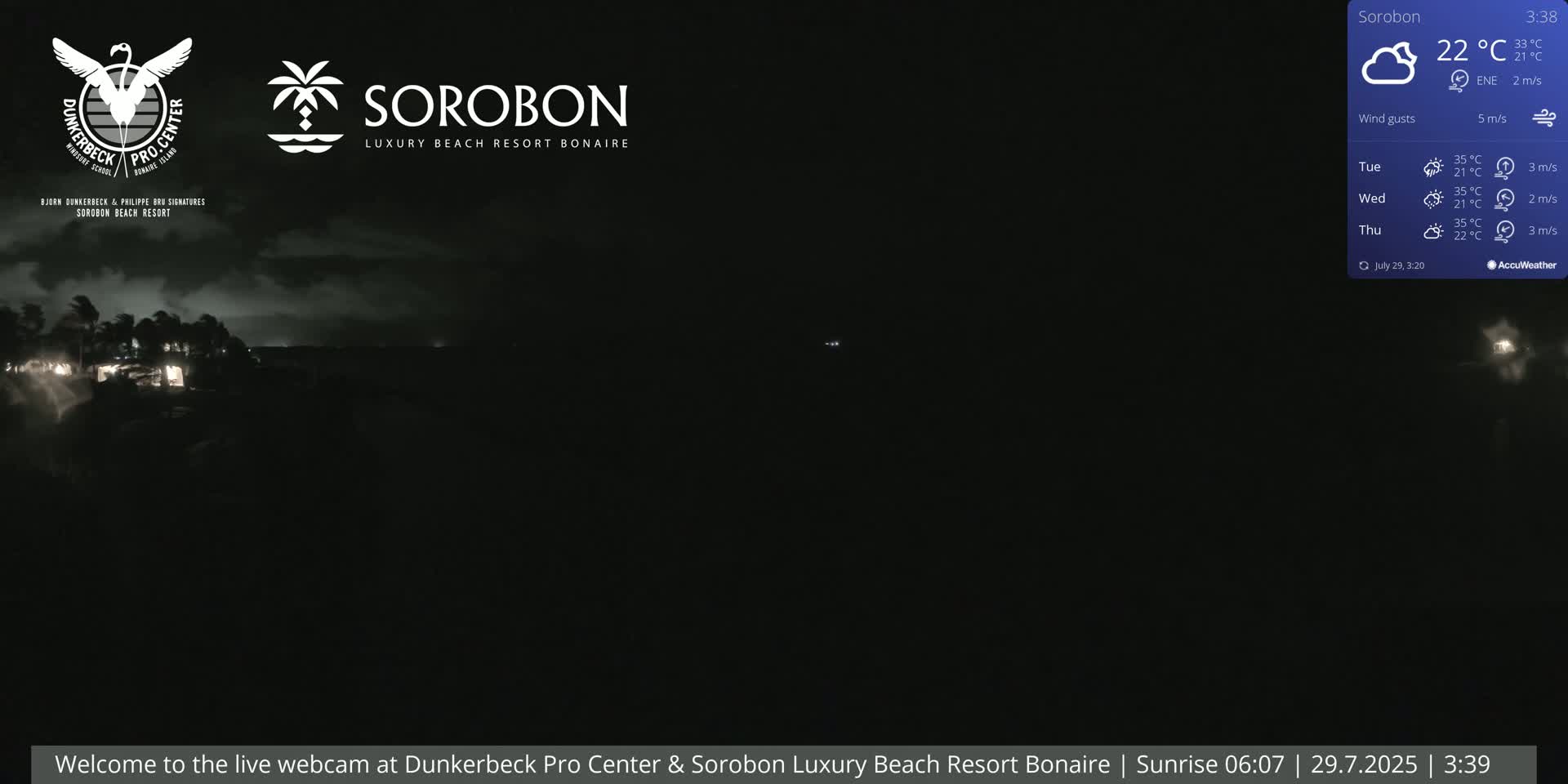 A nighttime, dark image shows a dimly lit shoreline with a few lights visible, under a cloudy sky with a slight wind.