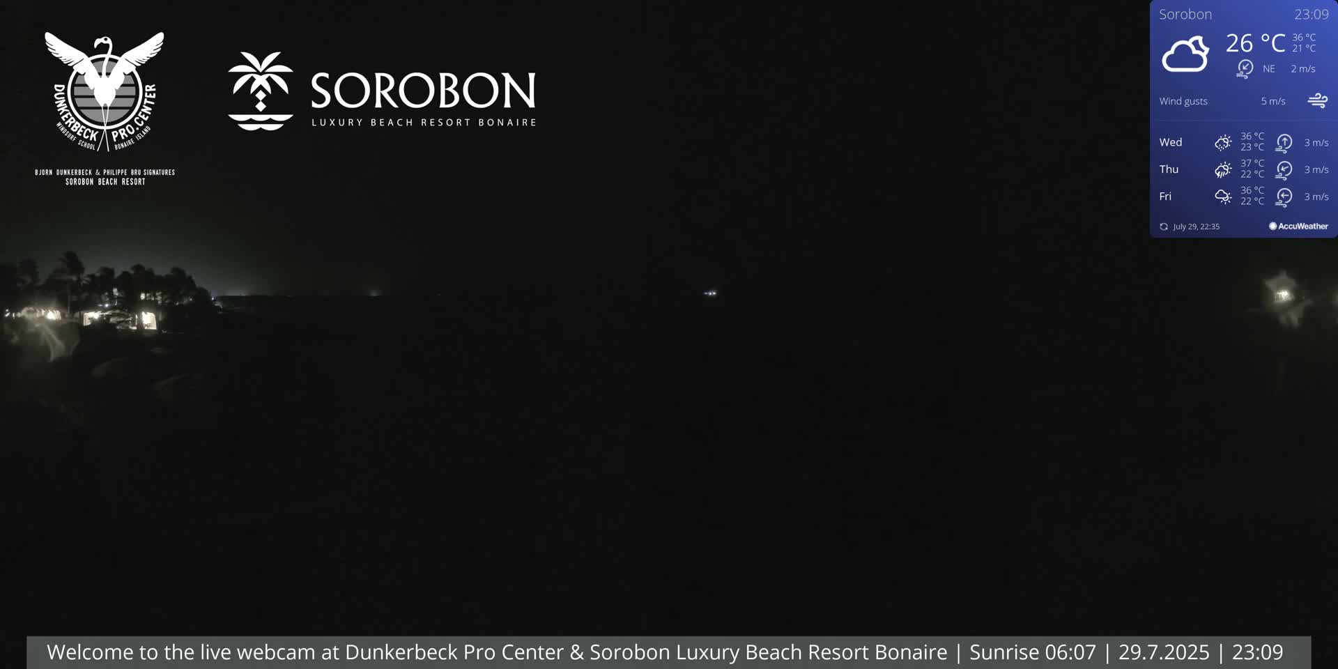 A nighttime, dark image shows a dimly lit shoreline with a few lights visible, under a cloudy sky with a slight wind.