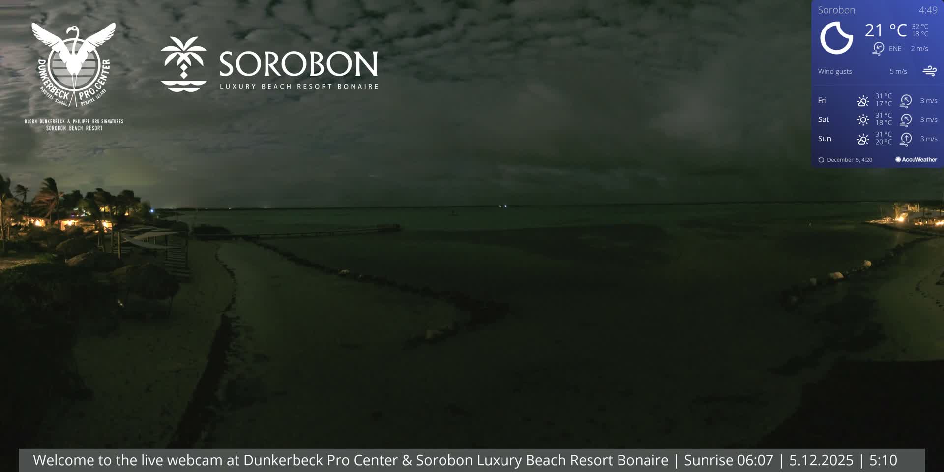 A cloudy, pre-dawn scene reveals a dimly lit tropical beach resort with illuminated palm trees and thatched umbrellas bordering calm water, extending towards a faint horizon.