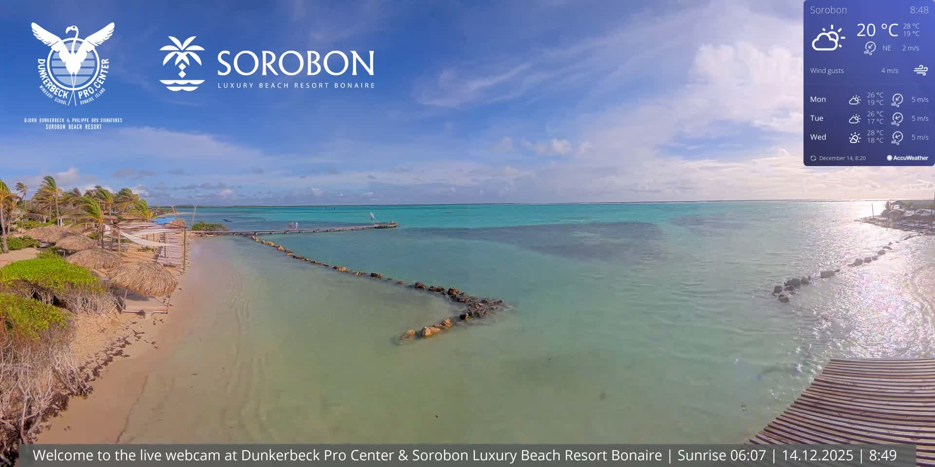 A cloudy, pre-dawn scene reveals a dimly lit tropical beach resort with illuminated palm trees and thatched umbrellas bordering calm water, extending towards a faint horizon.