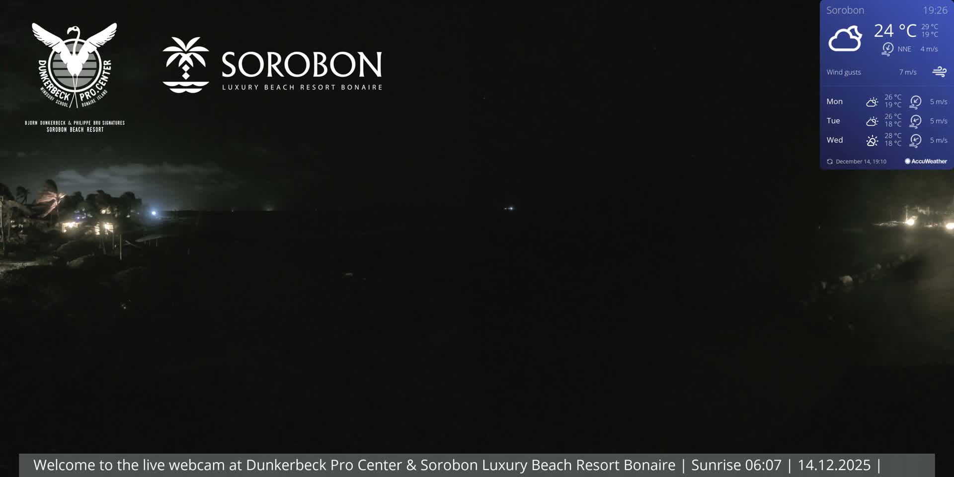 A cloudy, pre-dawn scene reveals a dimly lit tropical beach resort with illuminated palm trees and thatched umbrellas bordering calm water, extending towards a faint horizon.