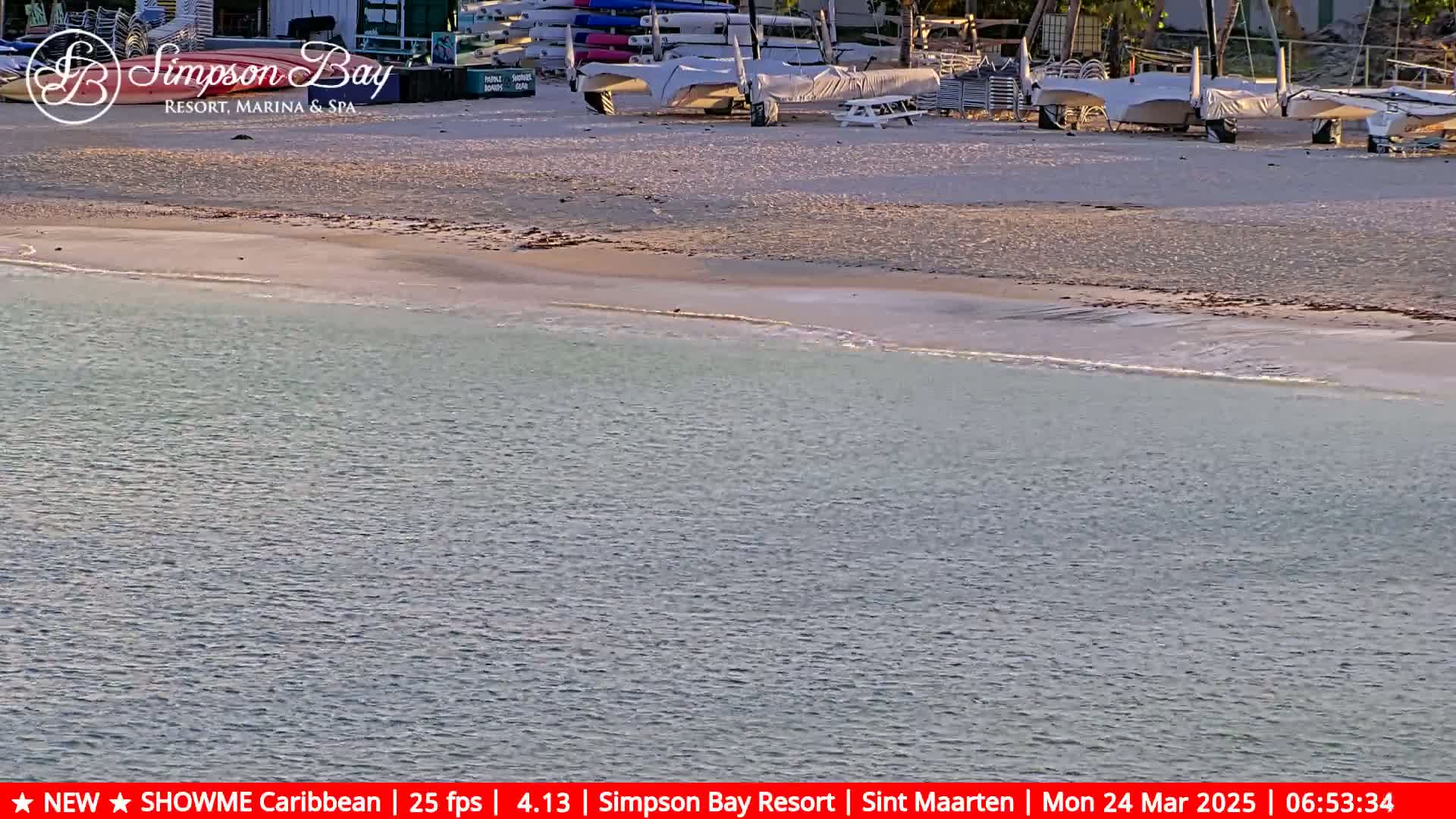 Several sailboats are beached on a sandy shore next to calm, light-blue water.