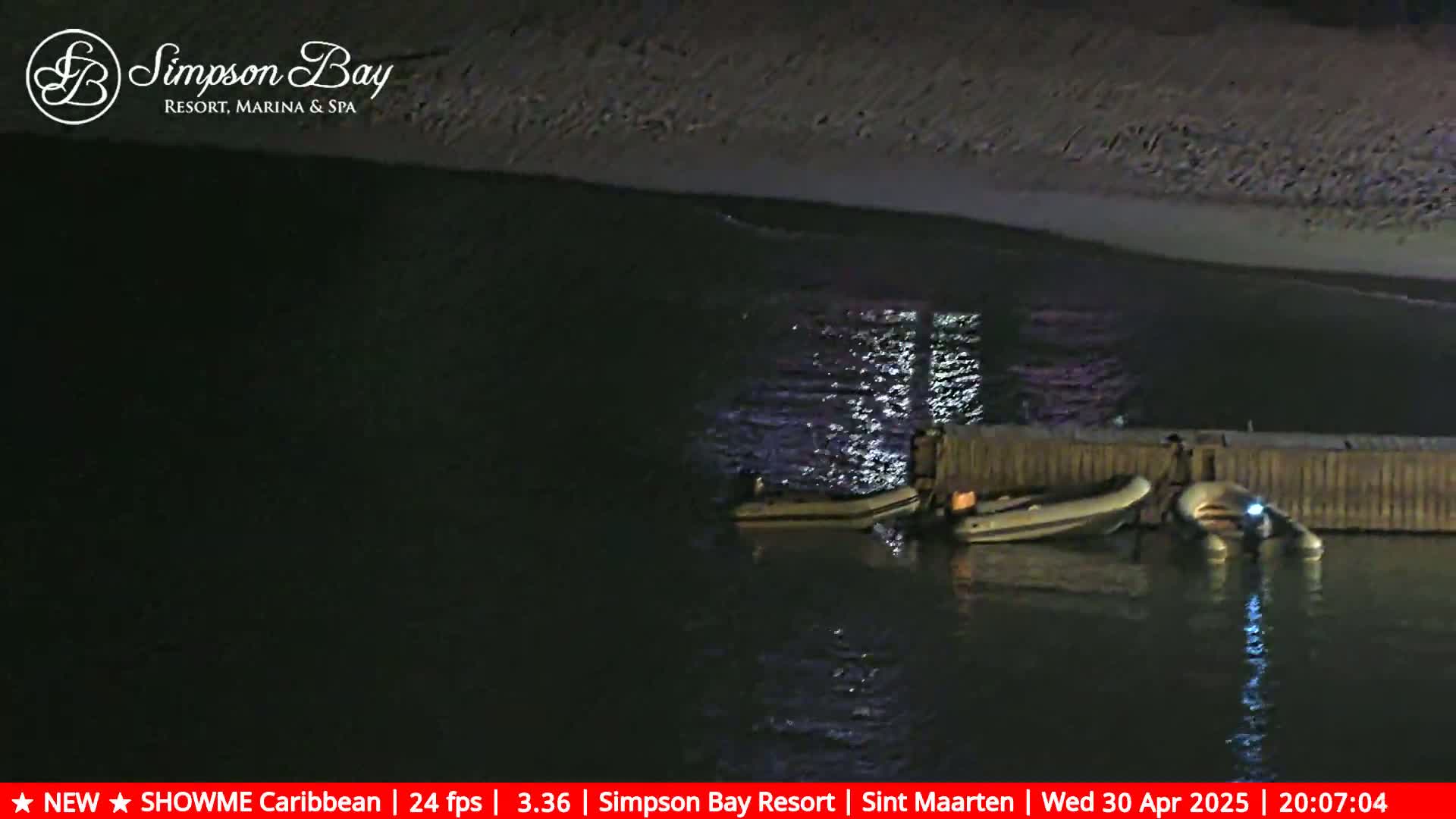 Several small inflatable boats are moored at a dark waterfront at night.