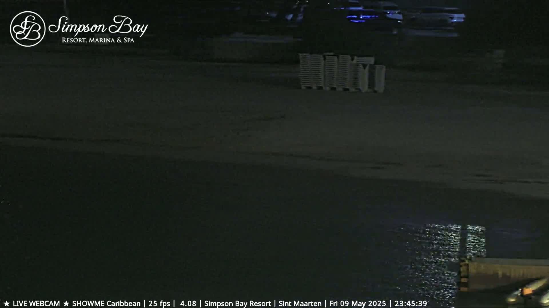 A dark, nighttime beach scene shows calm water reflecting light, with several white objects stacked near the shore.