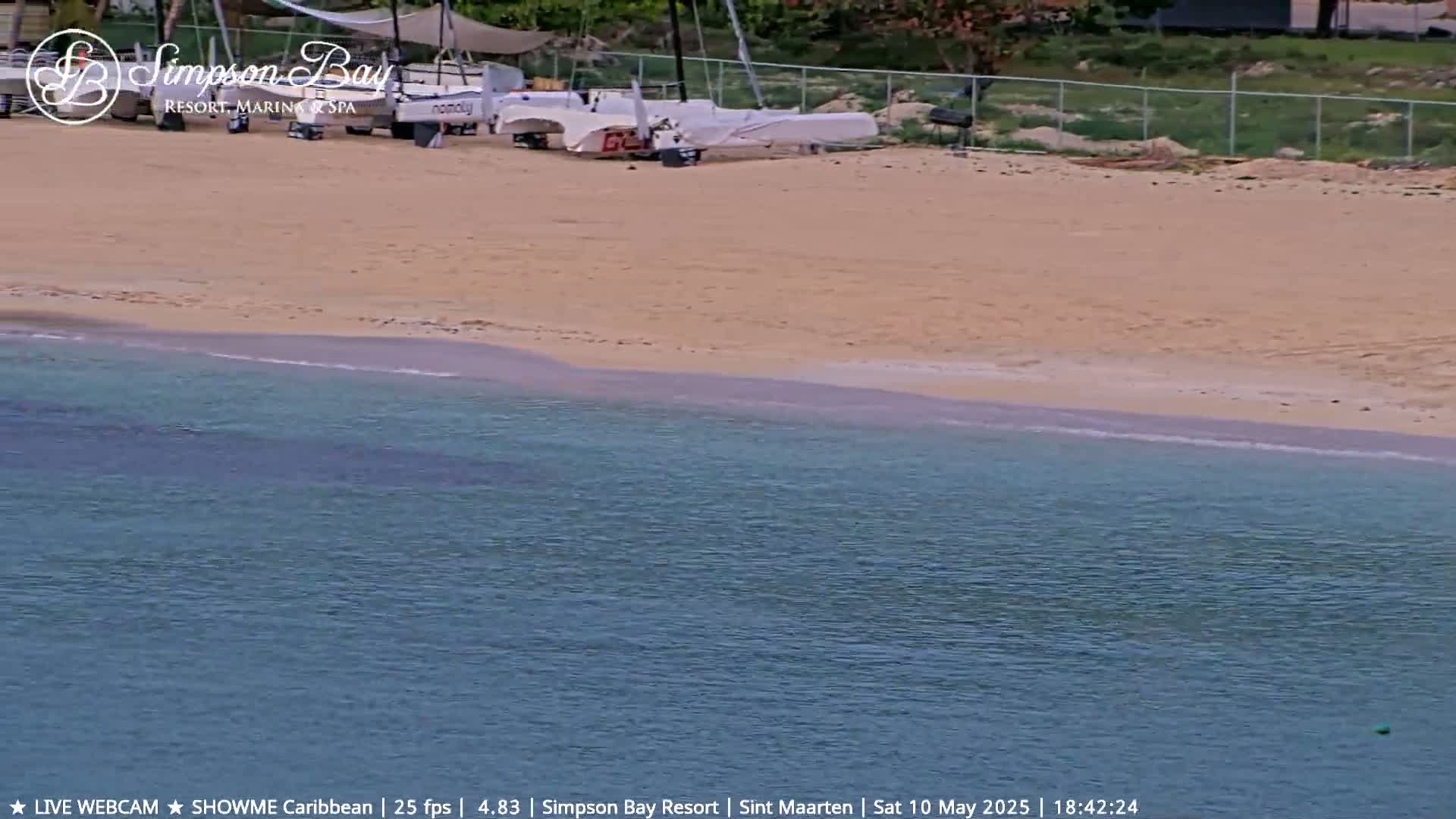 A sandy beach with several sailboats on the shore meets calm, turquoise water.