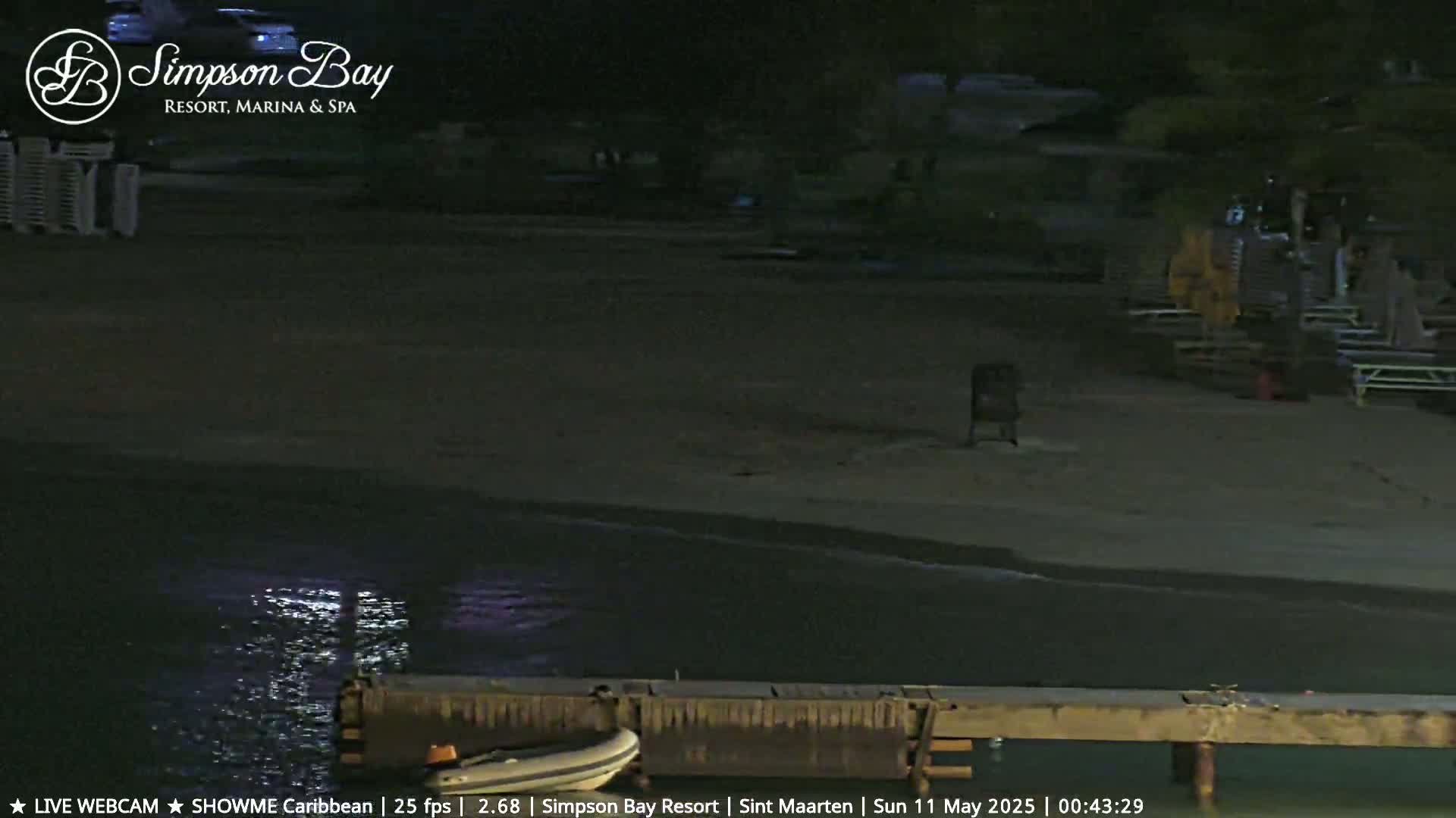 A nighttime view of a mostly empty beach with calm water lapping at a pier, a small boat is docked nearby.