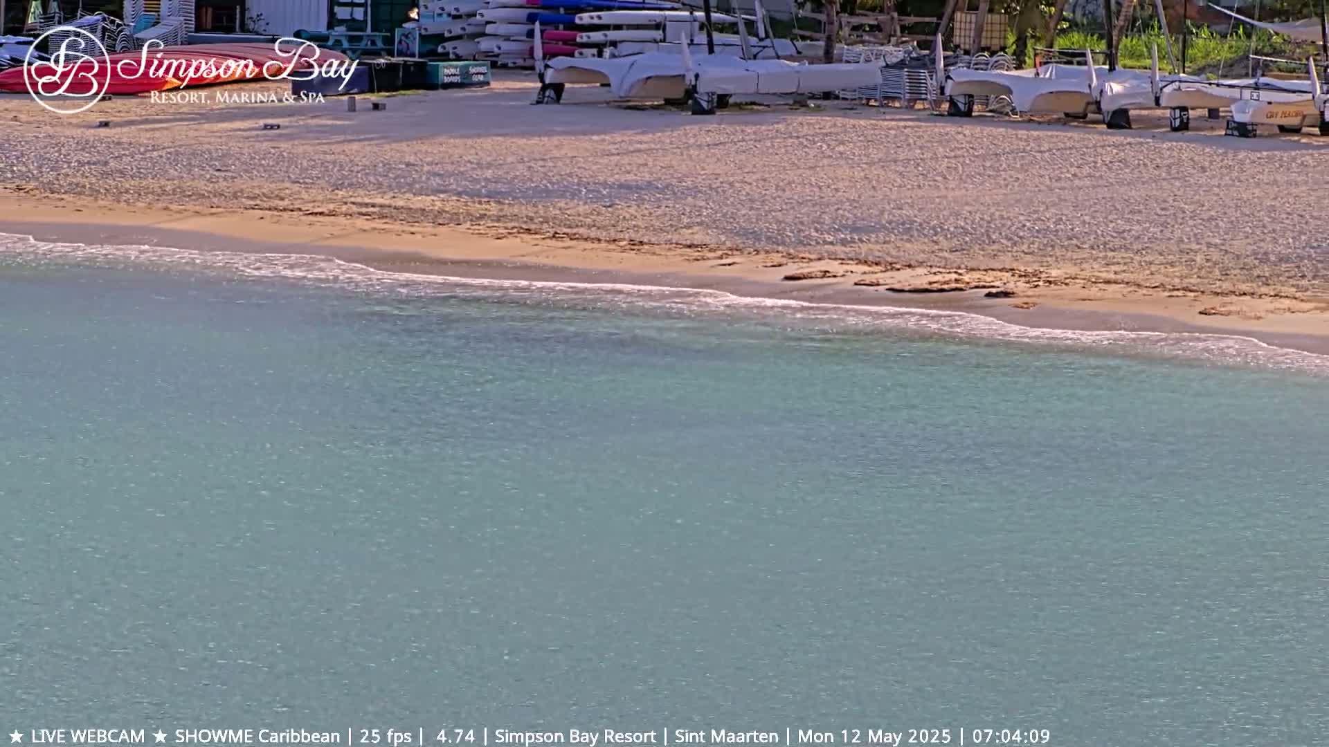 A sandy beach with several sailboats on shore meets calm, light-blue water.