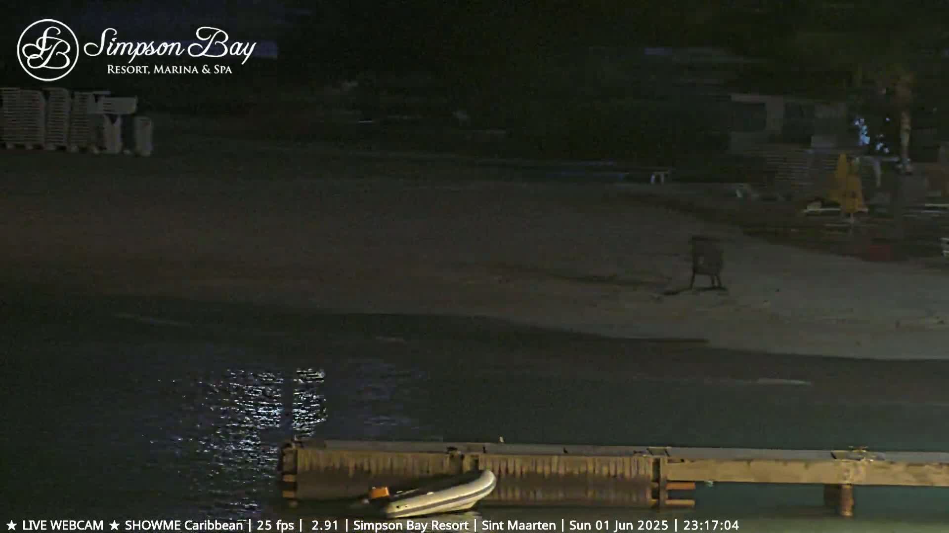 A dark, nighttime view of a beach with calm water, a small boat, and some beach furniture.