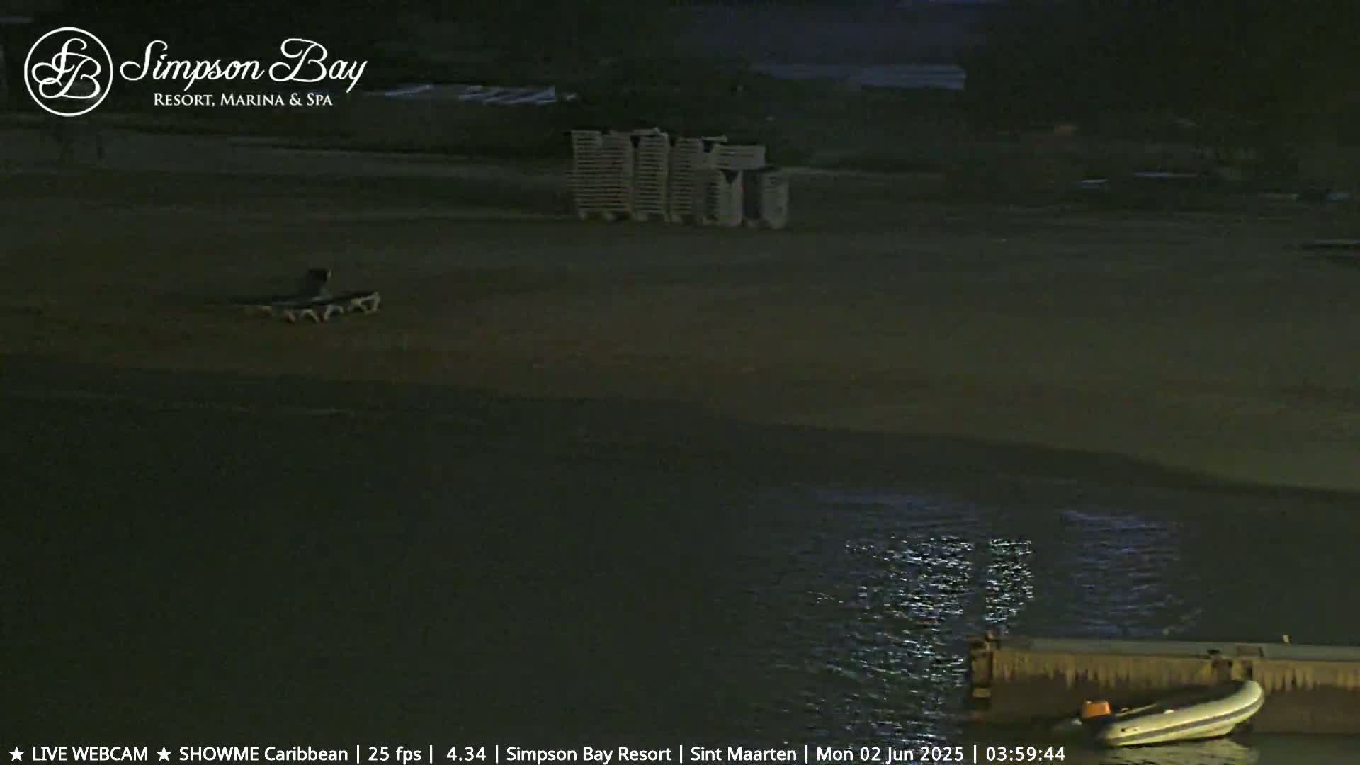 A dark beach at night is shown with a few lounge chairs and a small boat on the water.