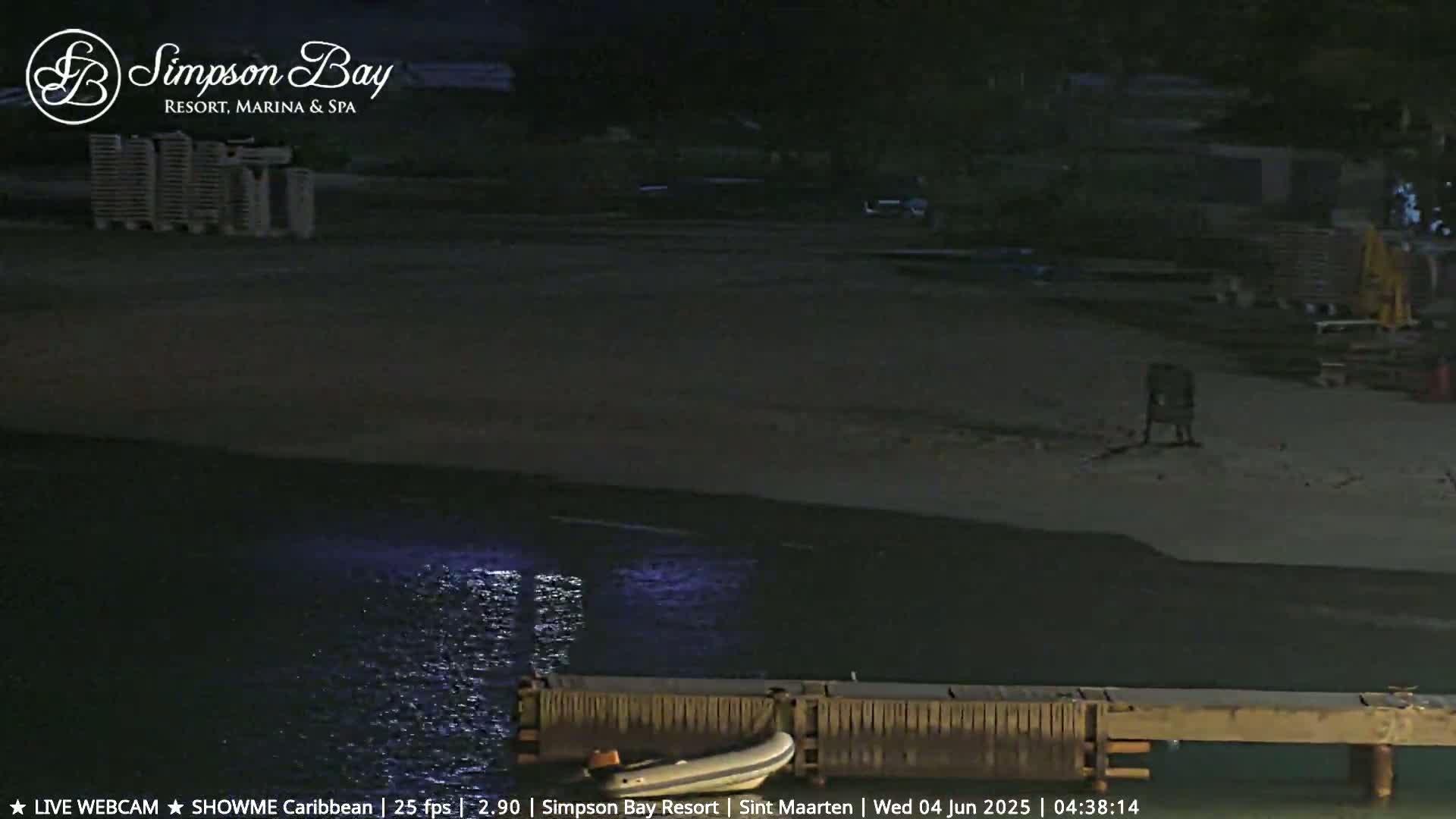 A dark, nighttime beach scene shows calm water lapping against a wooden dock with a small boat nearby.