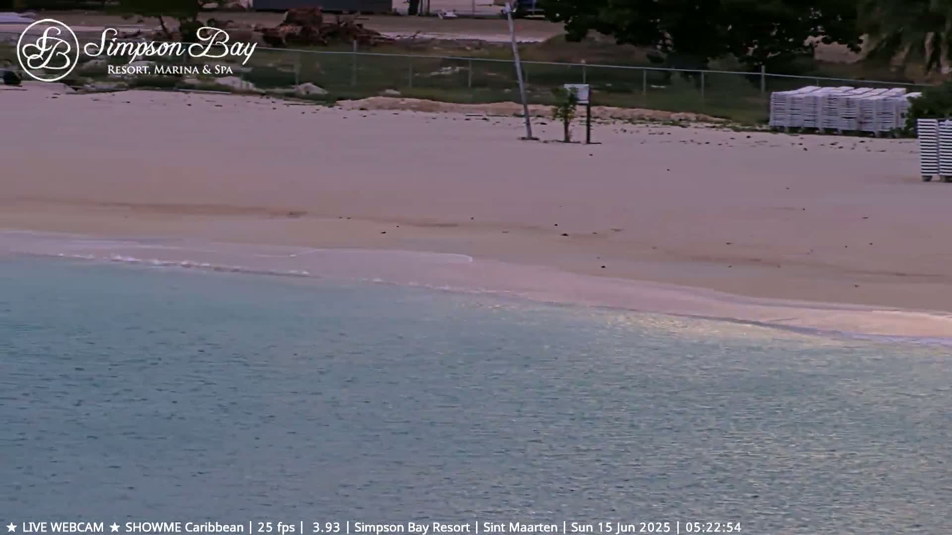 A tranquil beach with calm, light-blue water laps gently at the shore, under a soft, possibly early morning light.