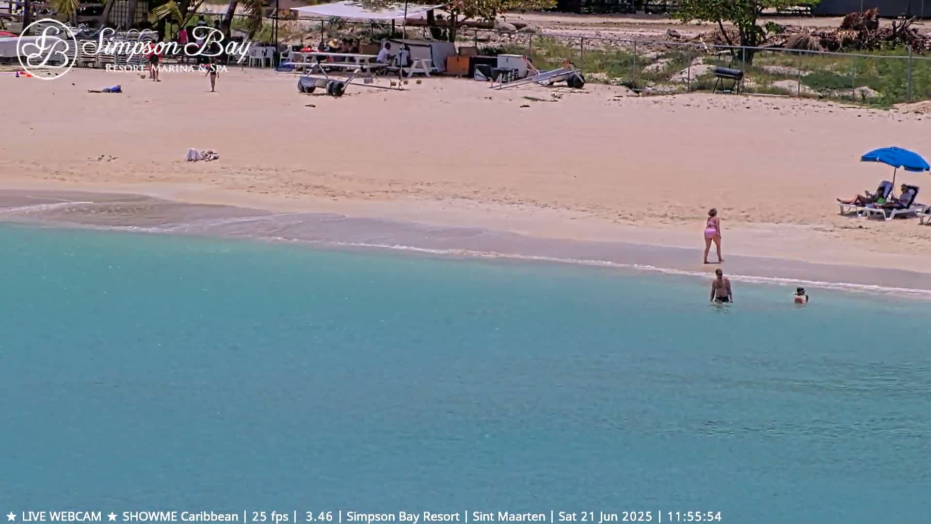 A sandy beach with turquoise water features several people sunbathing and swimming under a sunny sky.