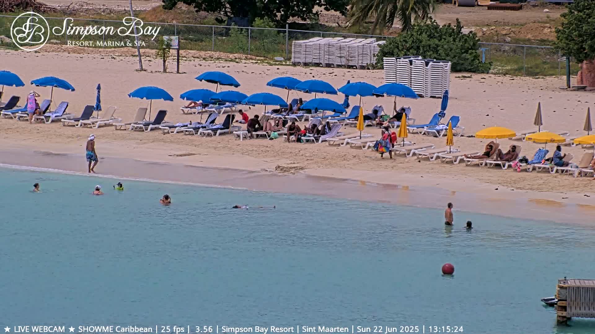 A sunny beach scene shows people relaxing on lounge chairs under umbrellas, others swimming in calm, clear turquoise water.