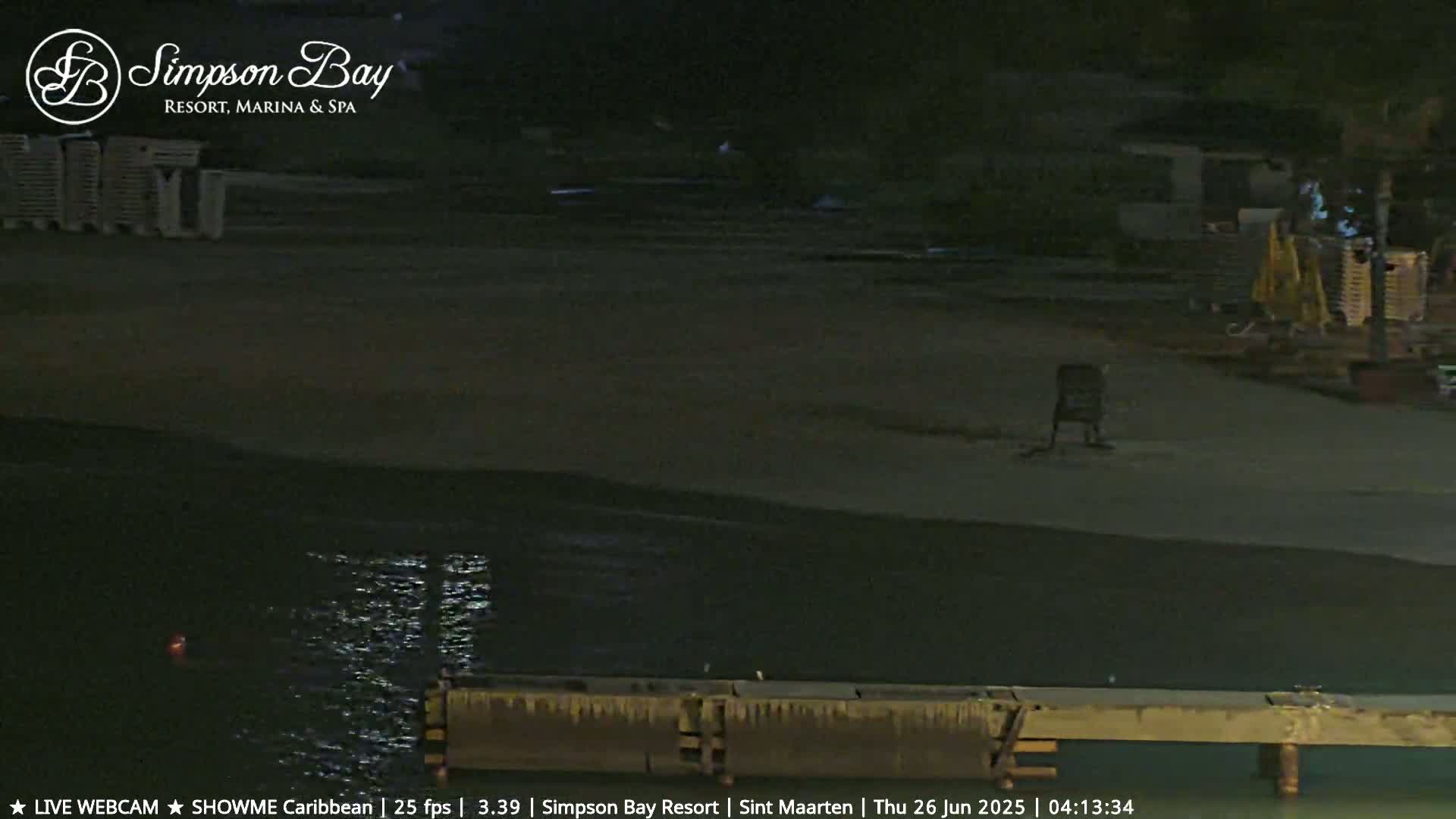 A dark, nighttime scene shows a mostly empty beach next to calm water with a low wooden dock.