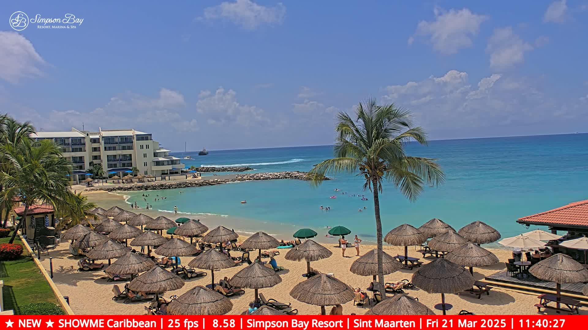 A sandy beach with numerous thatched umbrellas, lounge chairs, and people enjoying the turquoise water under a sunny sky.