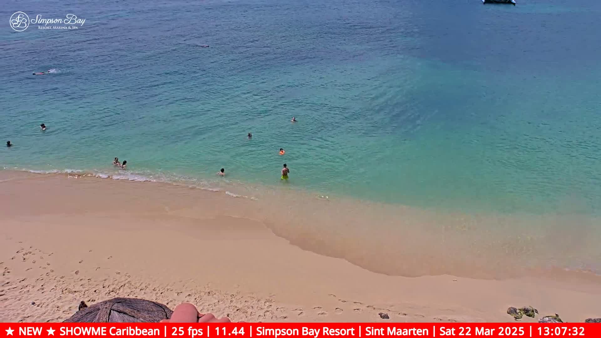 A sandy beach with calm, clear turquoise water and several people swimming.