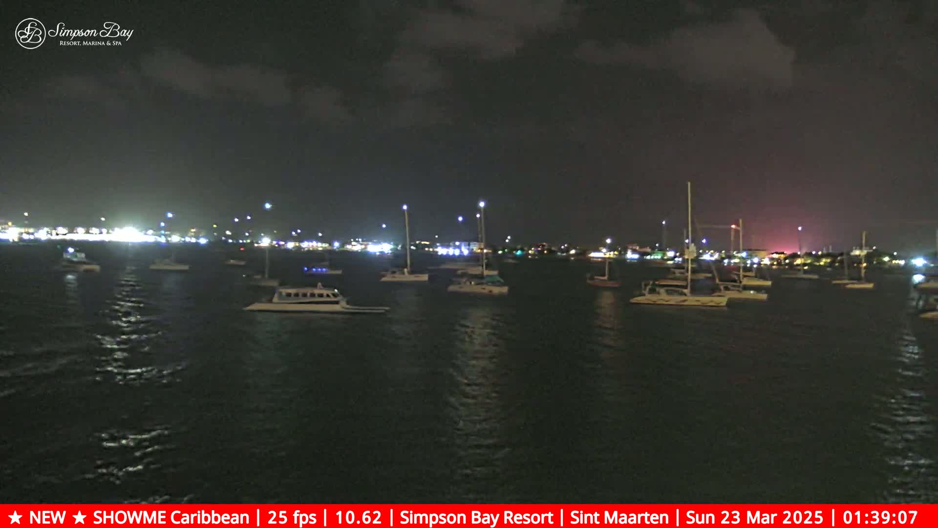 Many boats are moored in a dark bay at night under a cloudy sky.