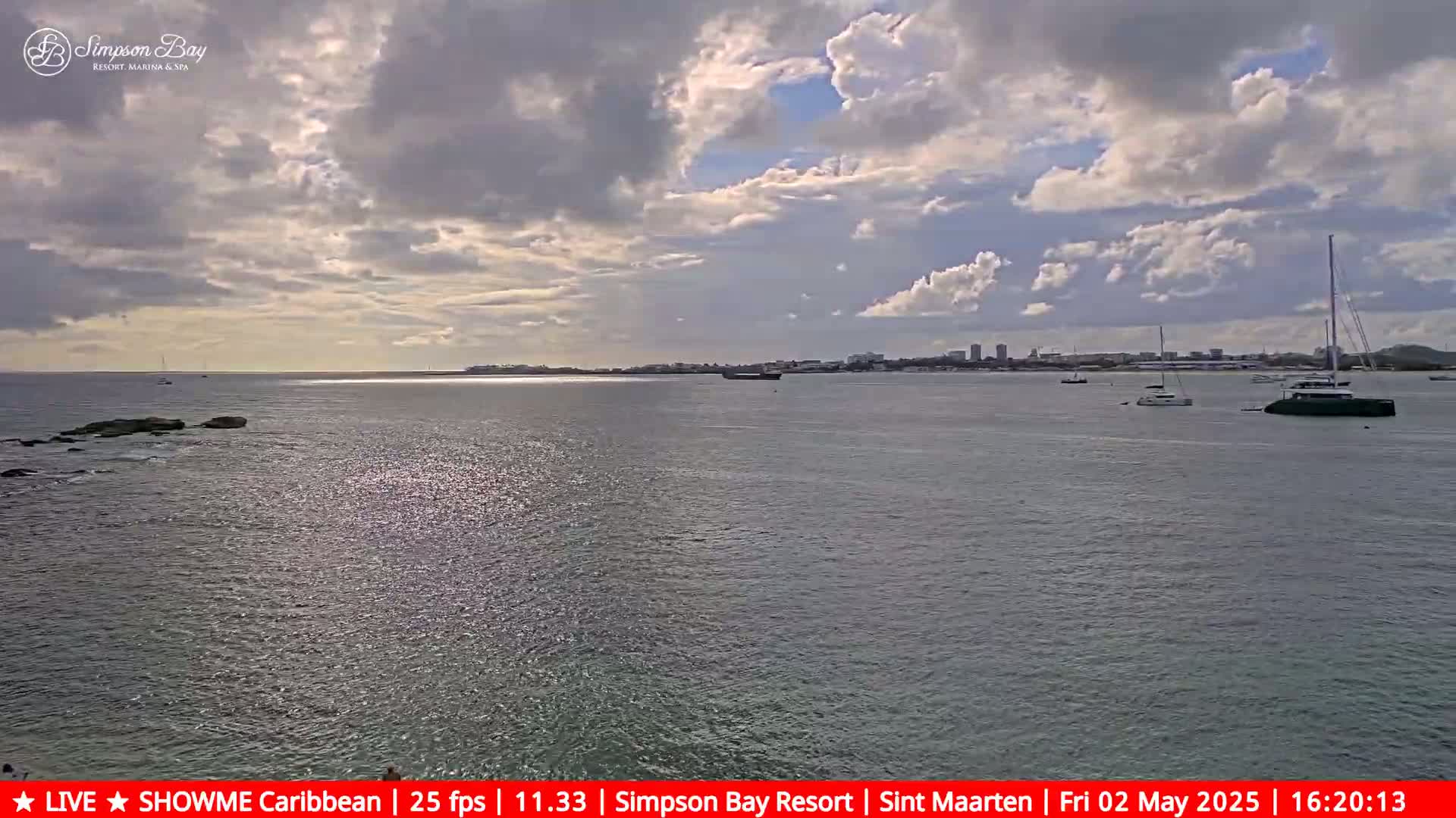 A partly cloudy day shows a calm body of water with several boats and a distant shoreline.