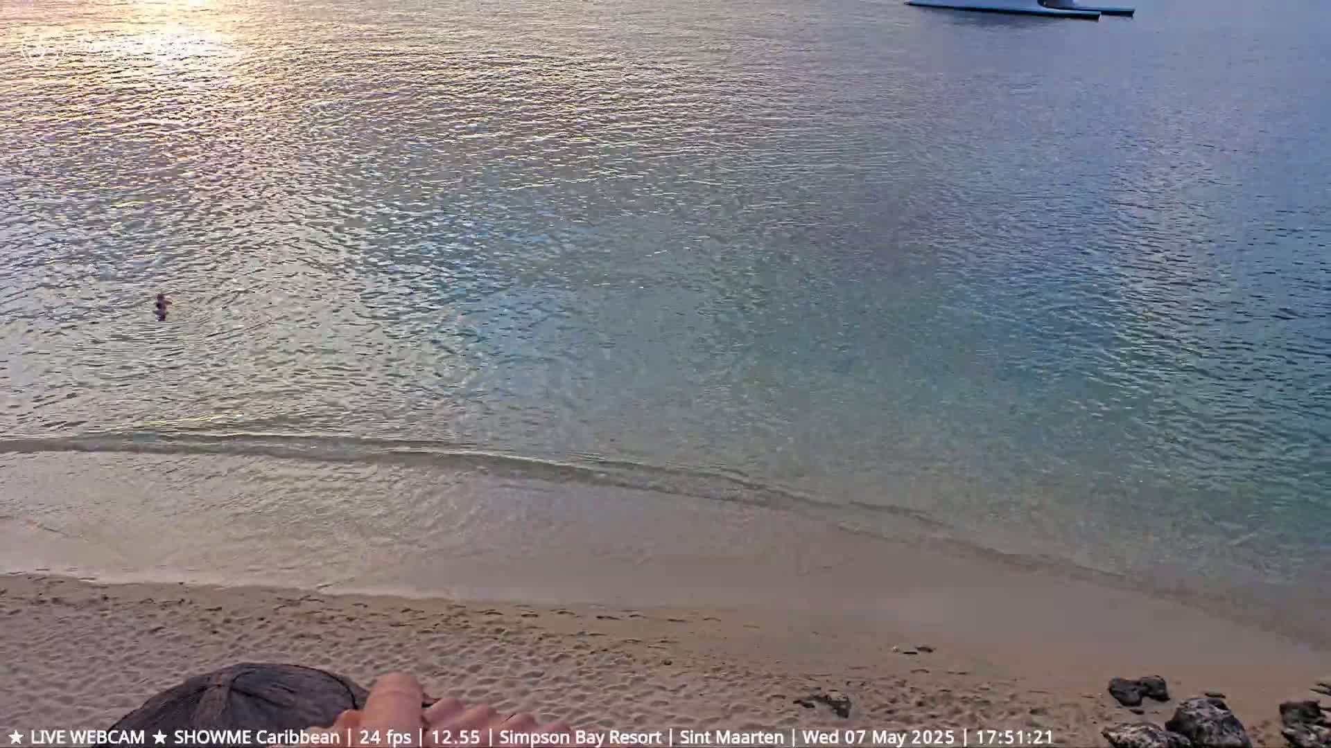 A person swims in calm, shallow, clear turquoise water near a sandy beach at sunset.