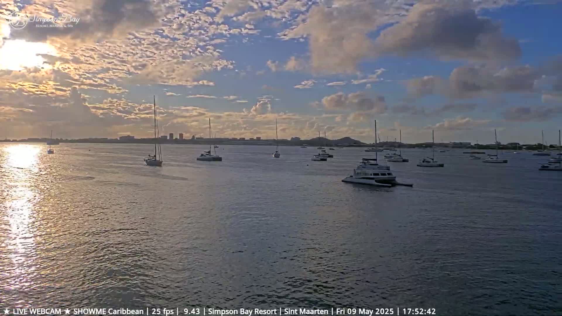 Numerous sailboats and motorboats are anchored in calm water under a partly cloudy sunset sky.