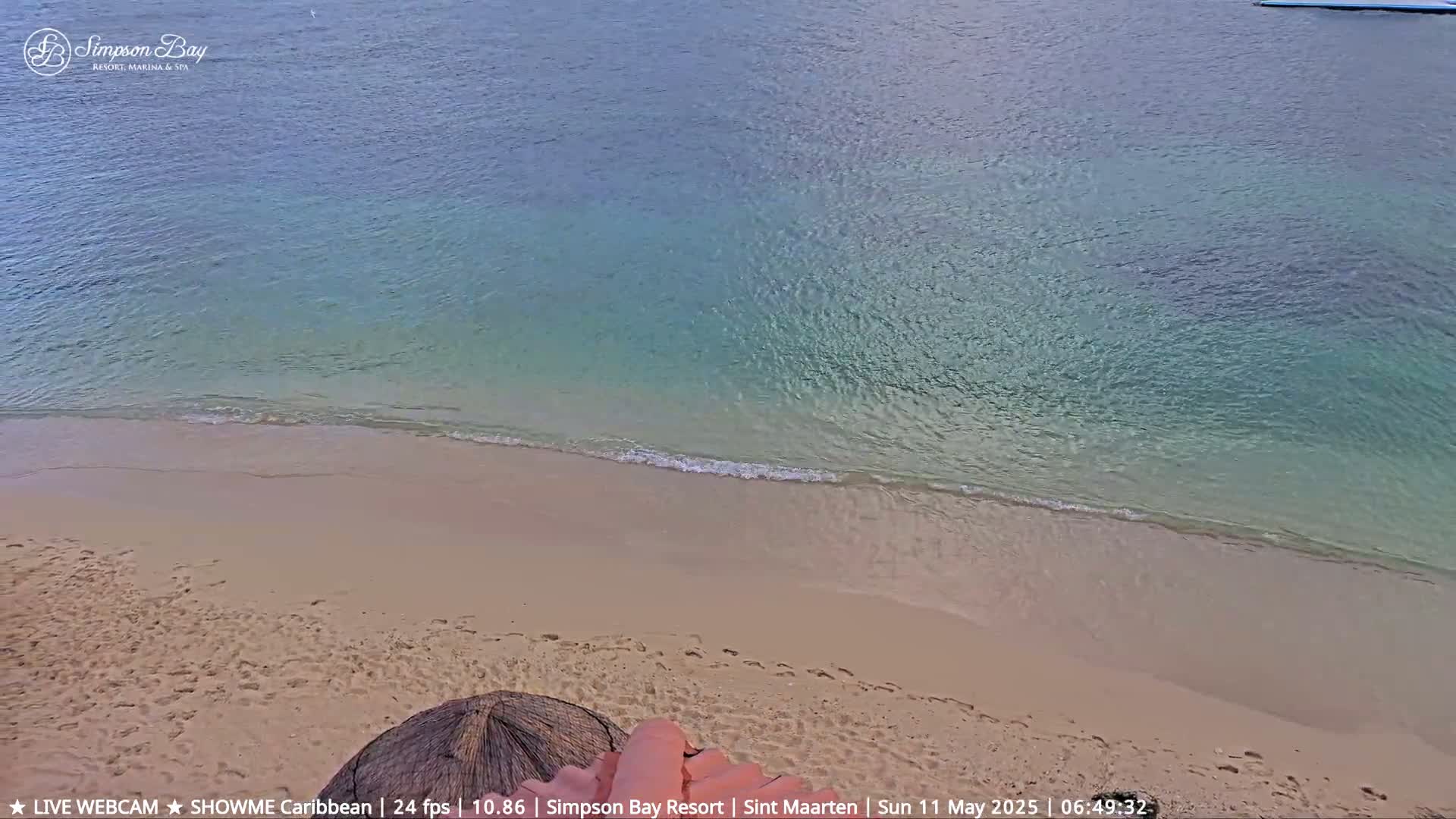 A sandy beach meets calm, shallow turquoise water under a sunny sky.