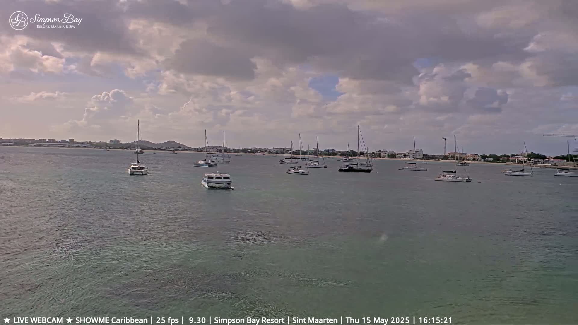 Several sailboats are moored in a calm bay under a partly cloudy sky.