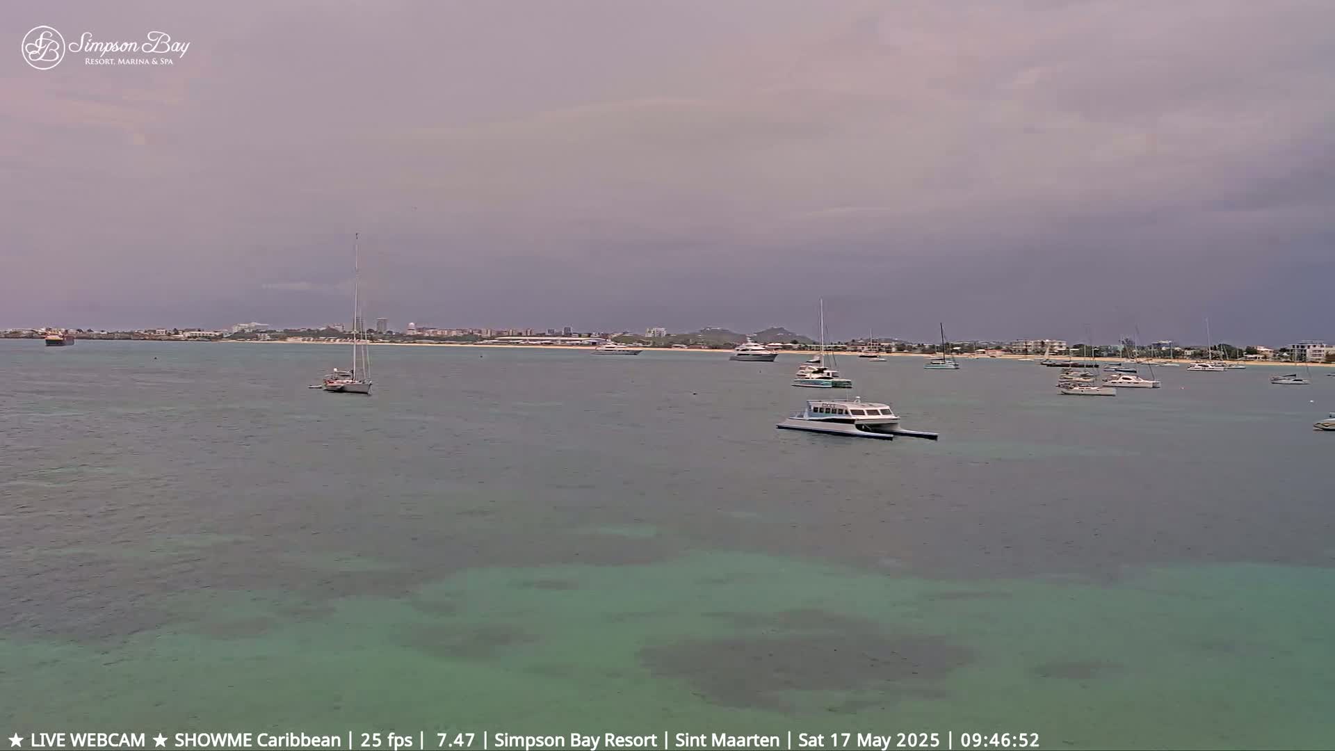 Several boats are anchored in a calm bay under an overcast sky.