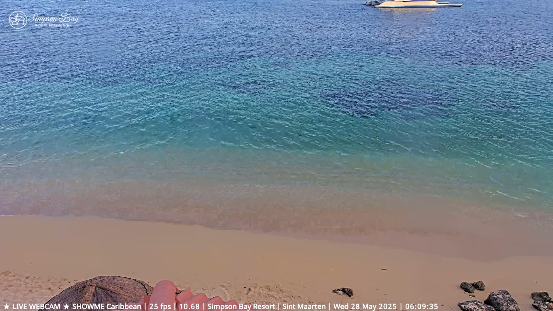 A sandy beach meets calm, shallow turquoise water under a clear sky.